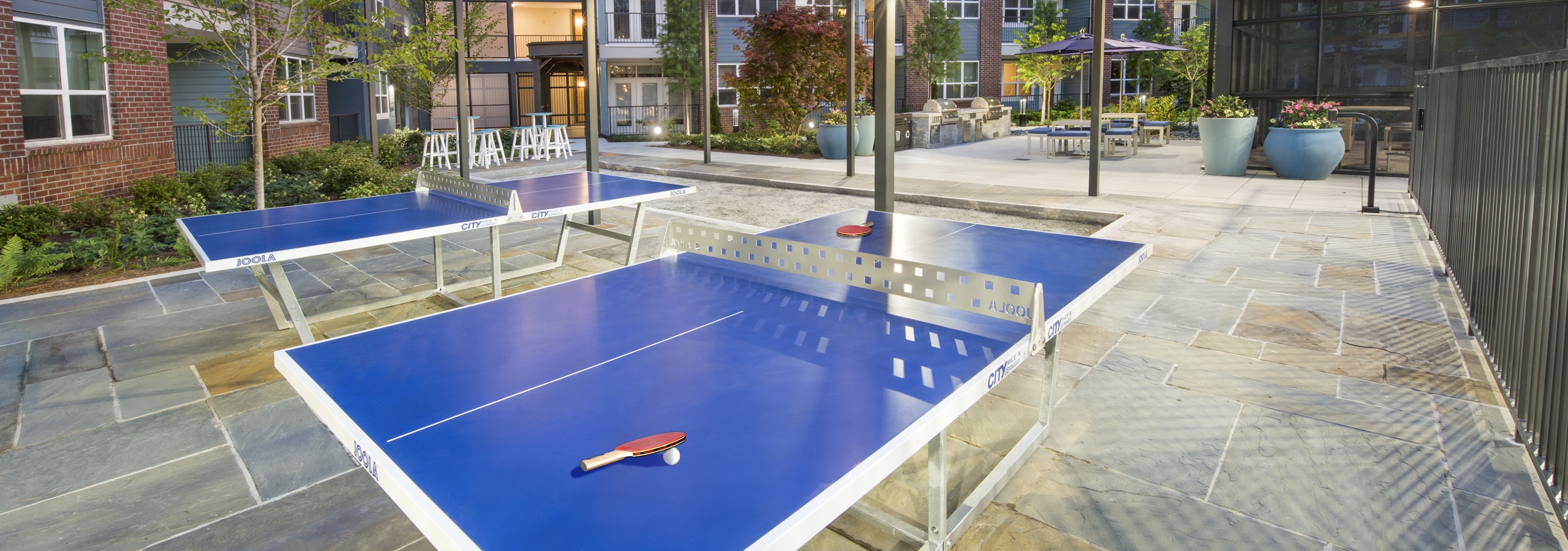 Evening view of ping pong area at AMLI Decatur with blue ping pong tables and hanging lights with seating areas in the back