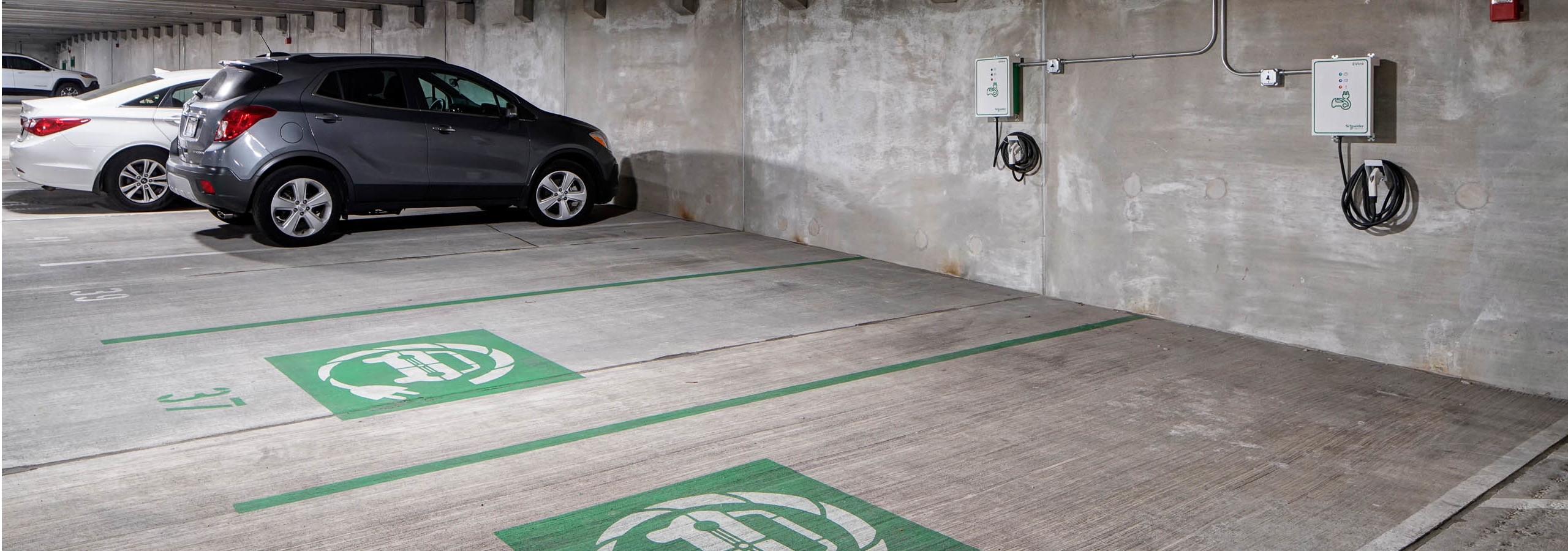 Interior of parking garage at AMLI Deerfield with electric car charging stations and gray and white cars in adjacent spaces