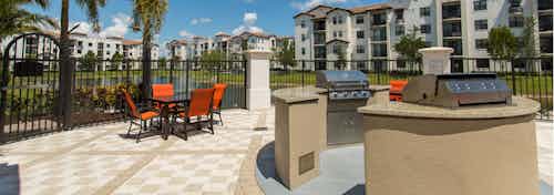 View in the daylight of AMLI Doral barbeque area with built in barbeques and orange outdoor seating, overlooking the lake