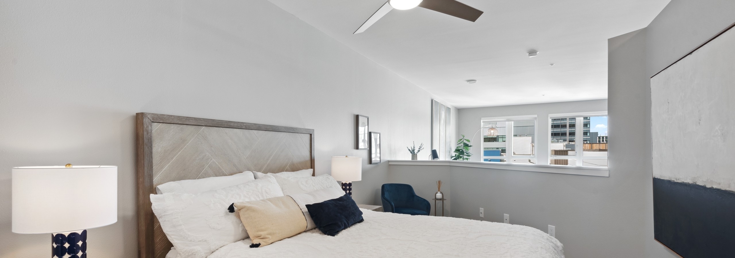 AMLI 535 bedroom with light wood bed and nightstand with while bedspread and half wall over looking view to the city