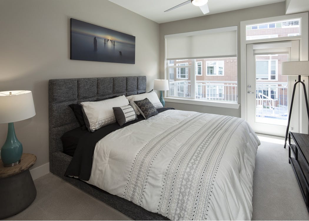 Interior view of AMLI Riverfront Green apartment bedroom and lamps with window views of adjacent brick apartment building