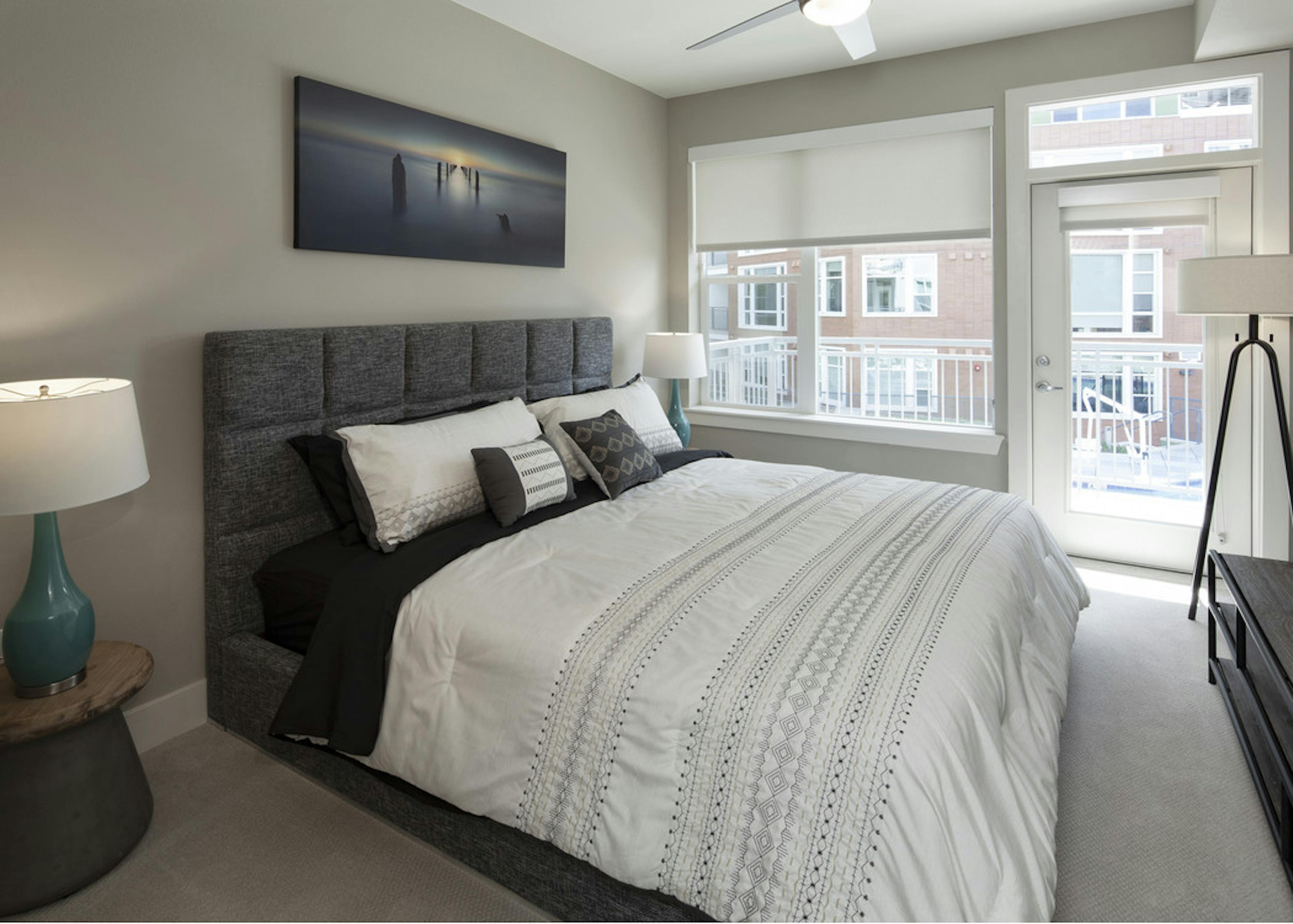 Interior view of AMLI Riverfront Green apartment bedroom and lamps with window views of adjacent brick apartment building