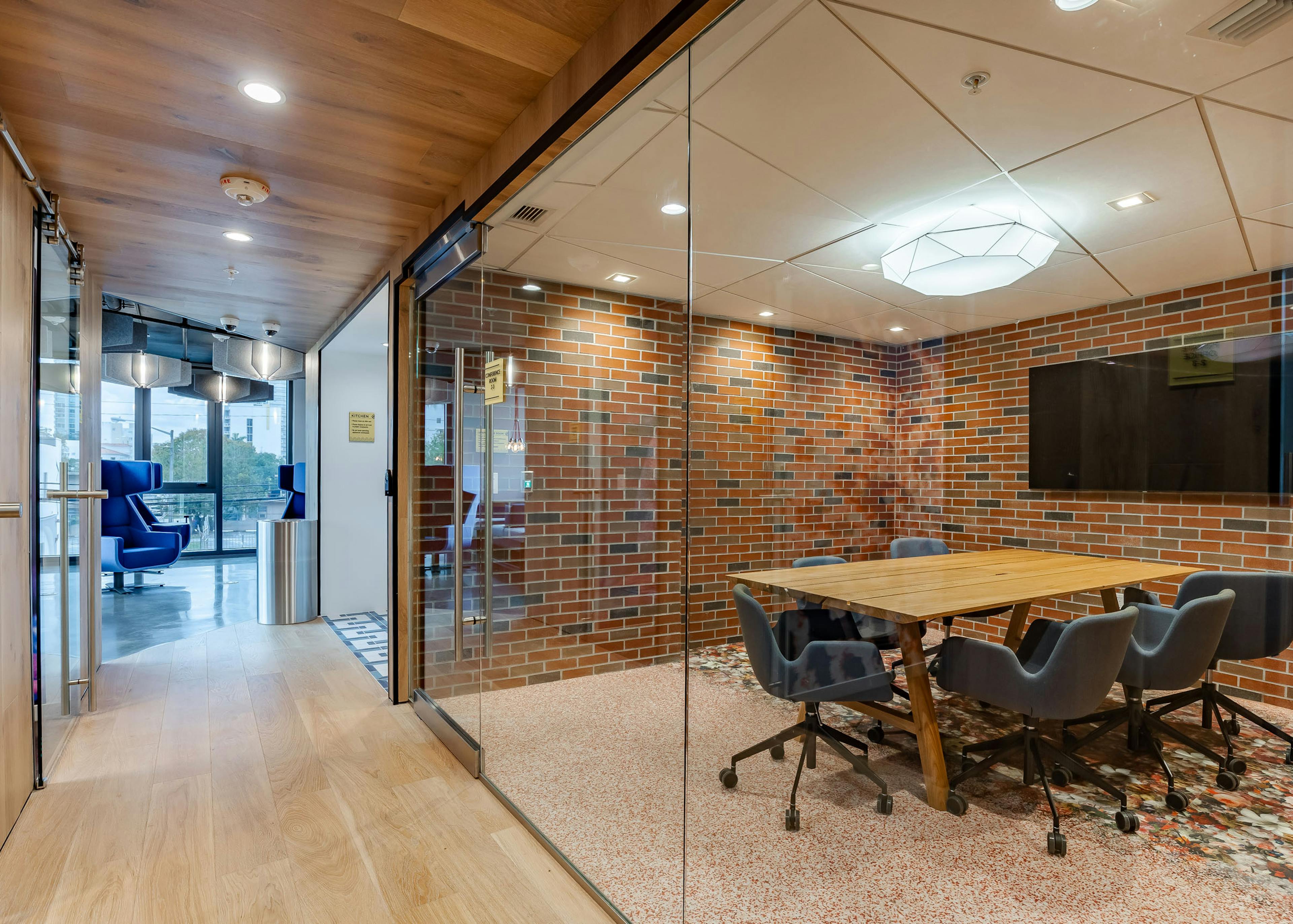 Glass enclosed conference room at AMLI Midtown Miami with wood table and 6 chairs and TV on and brick wall and adjacent hallway