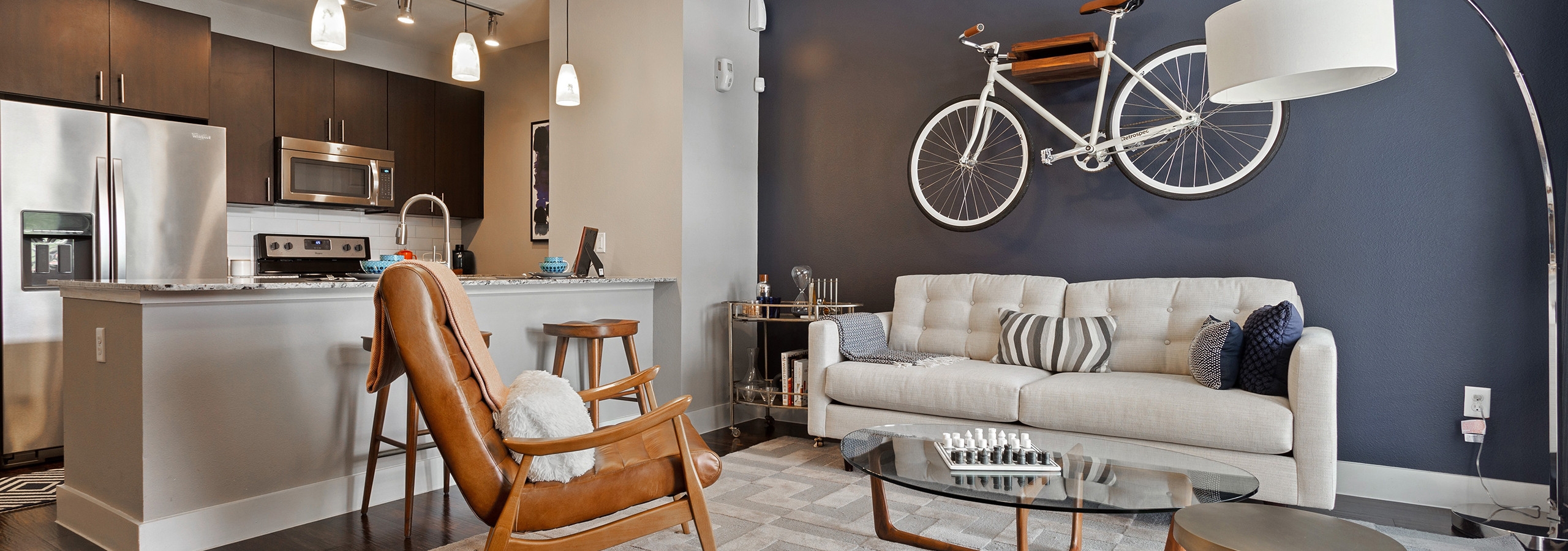 Interior view of AMLI Covered Bridge living area with a blue accent wall and pendant lighting in the kitchen