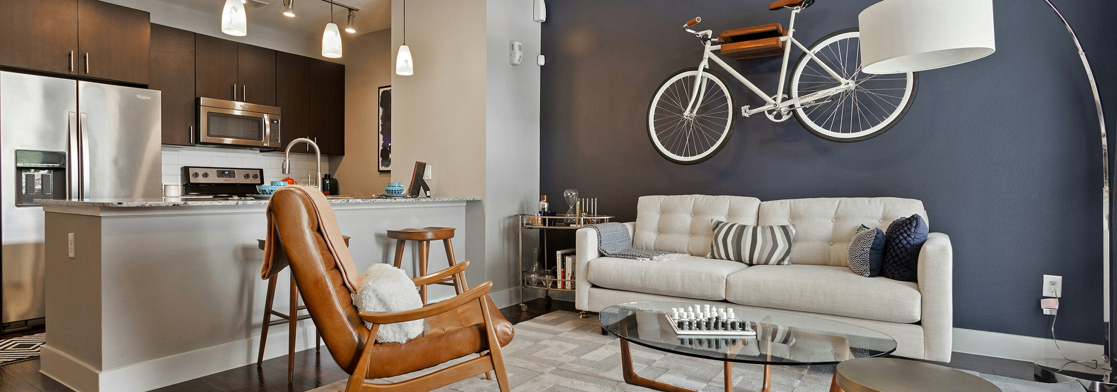 Interior view of AMLI Covered Bridge living area with a blue accent wall and pendant lighting in the kitchen