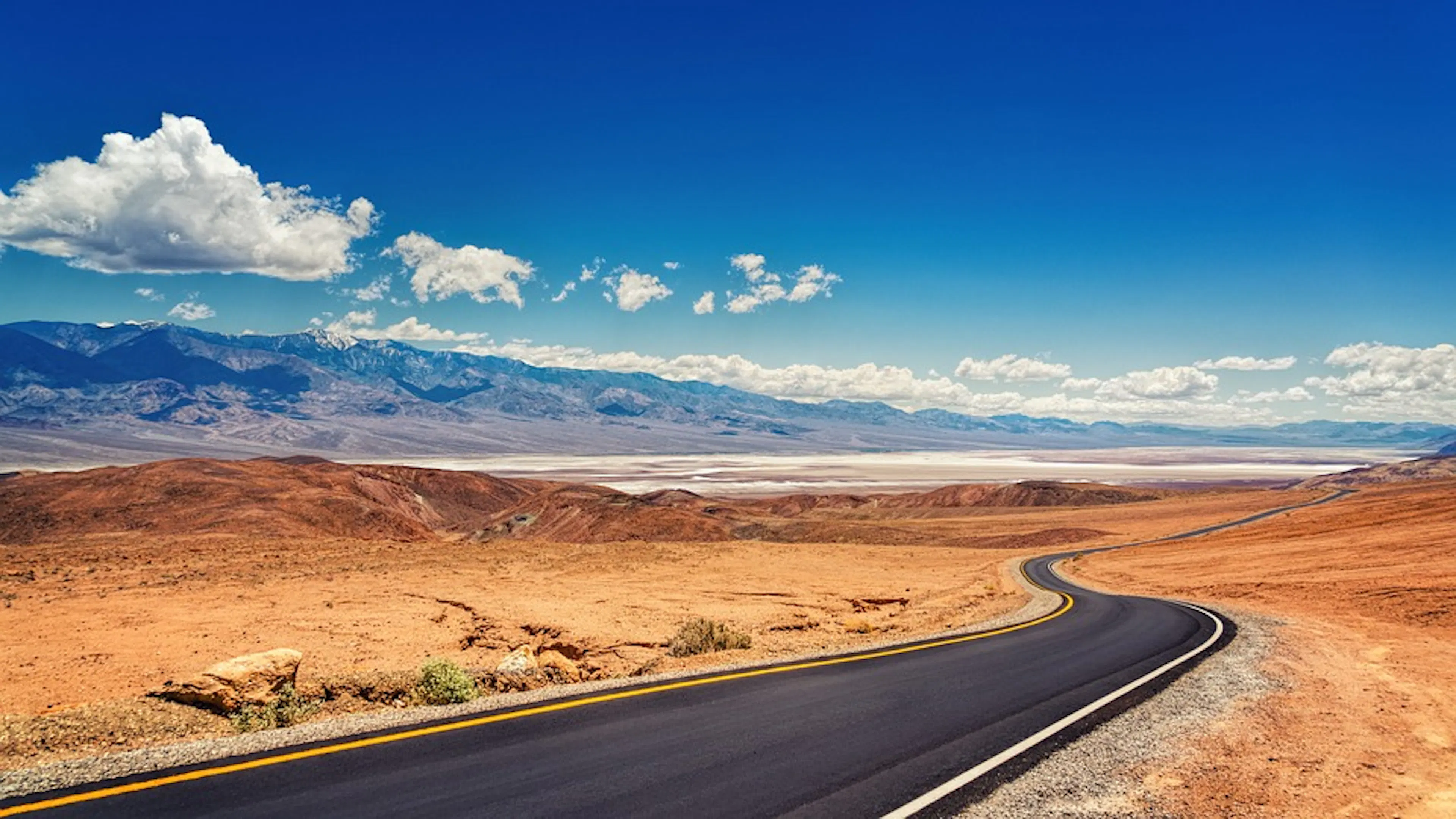 An empty asphalt road winding through the red dusty sands of Death Valley National Park
