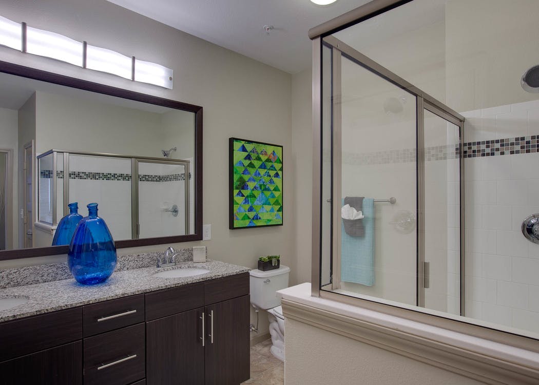 AMLI Ponce Park bathroom with double vanity with granite countertops with a toilet and a white shower tub with sliding doors