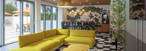 Lounge at AMLI Midtown Miami apartments with yellow modern furniture and black and white tile floor and wall of windows