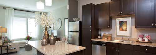 AMLI 5350 island kitchen with dark wood cabinets and granite countertops with peek into living area and window in background