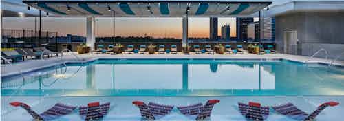 View from rooftop pool at AMLI Arts Center at sunset with lounge chairs in shallow water and the sky reflecting on the water