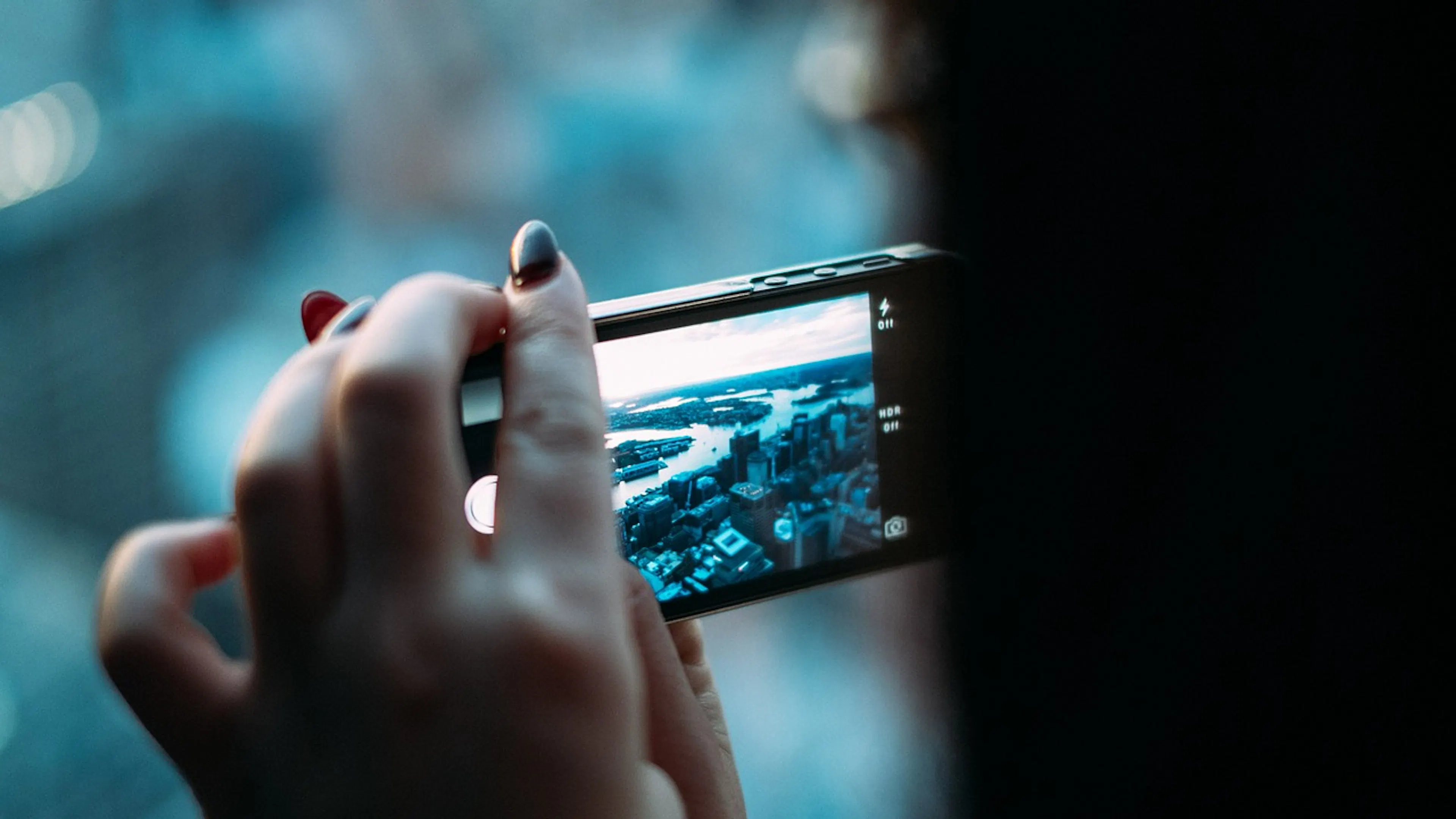 A womans hand holding an iPhone horizontally and taking a picture of a city