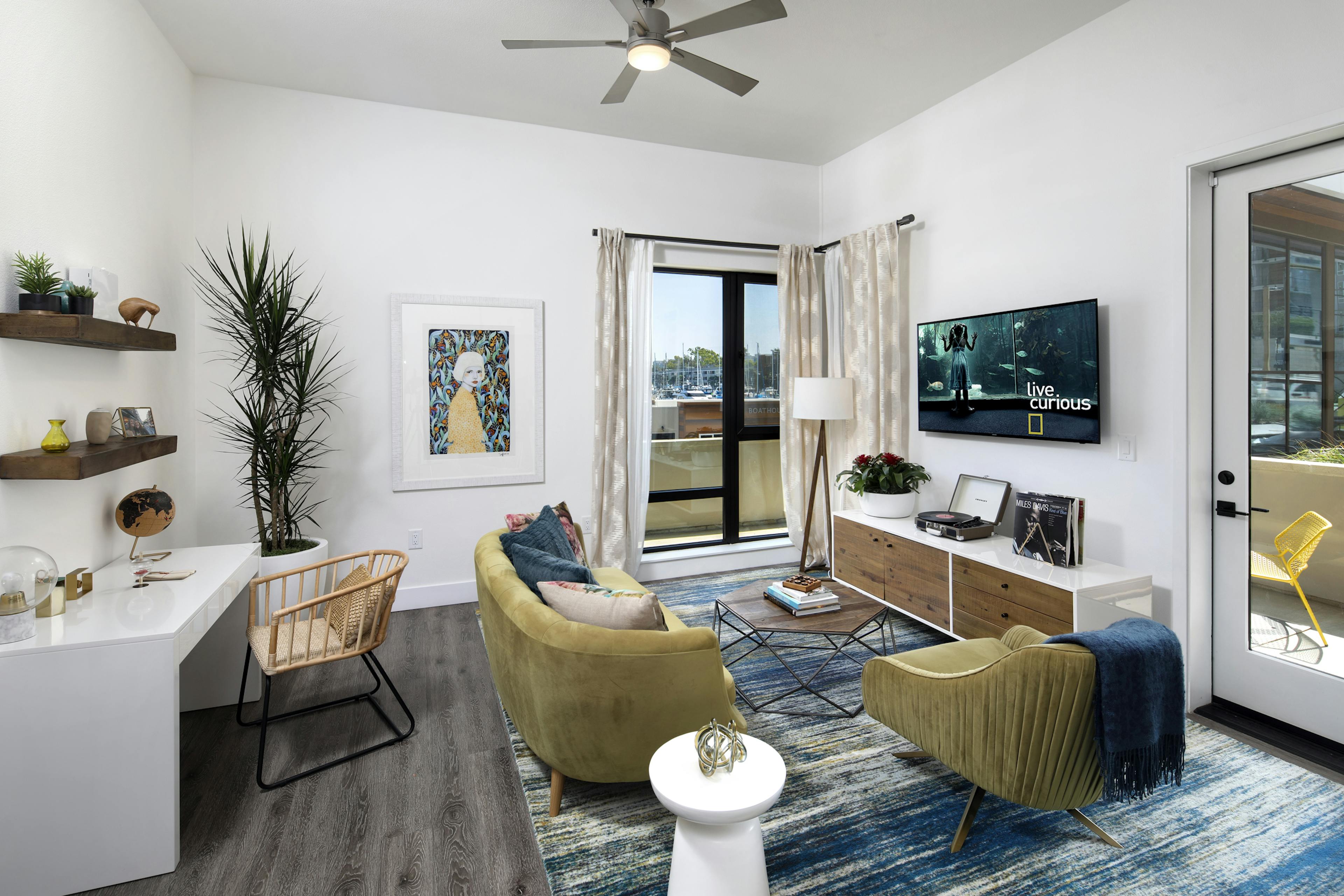 Interior of AMLI Marina Del Rey model living room with couch, coffee table and desk in front of large window facing marina