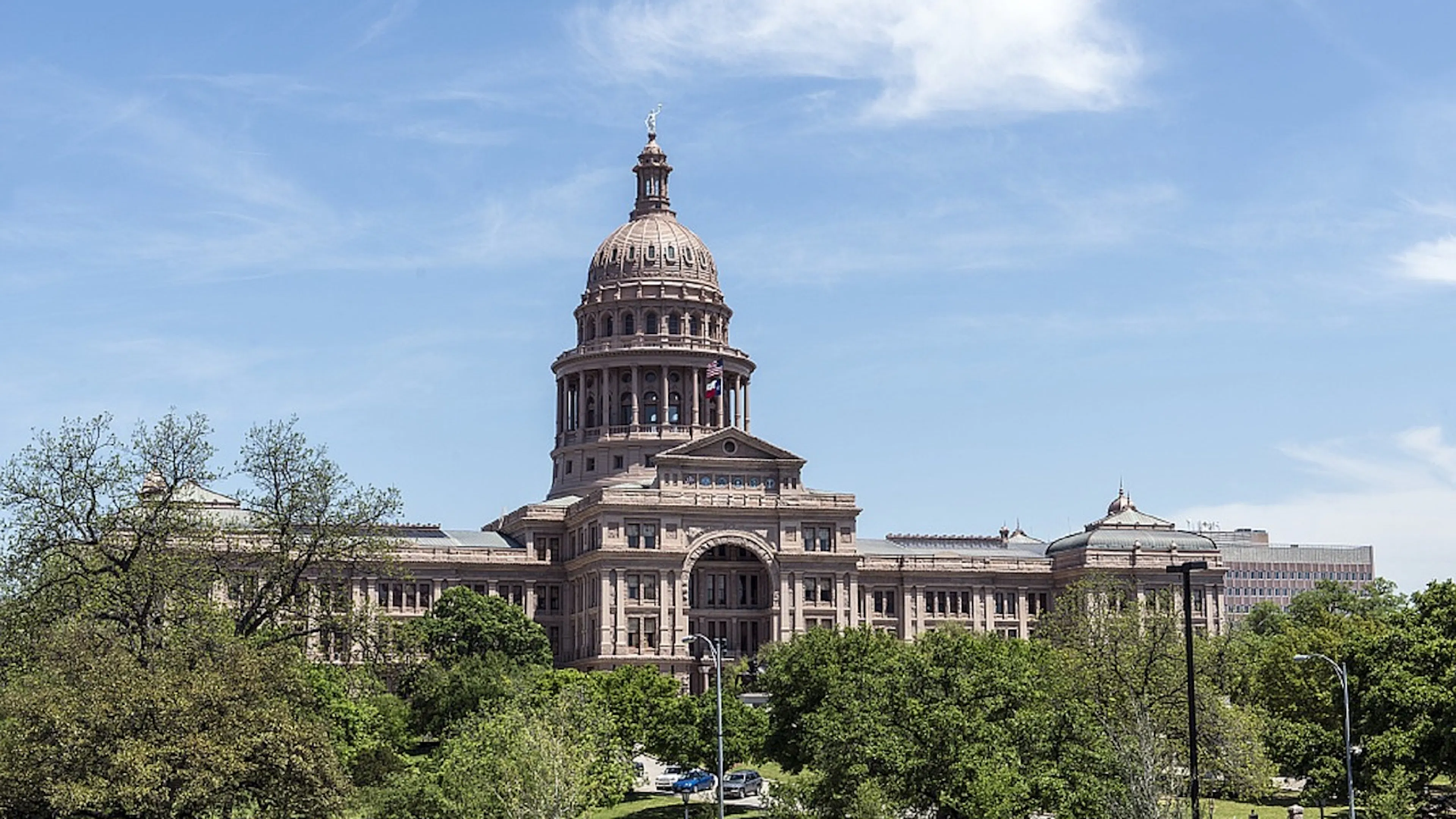 A wide angle shot of the ornate red Texas State Capitol building with some trees in the foreground