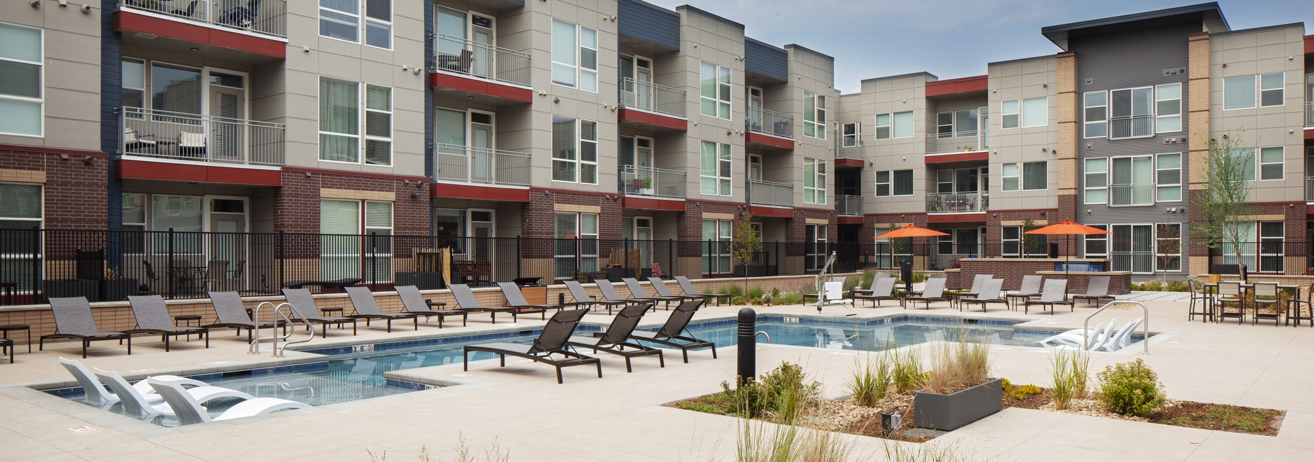 Landscaped courtyard pool area at AMLI Littleton Village with lounge chairs inside and along pool edge and orange umbrellas