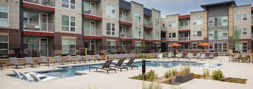 Landscaped courtyard pool area at AMLI Littleton Village with lounge chairs inside and along pool edge and orange umbrellas