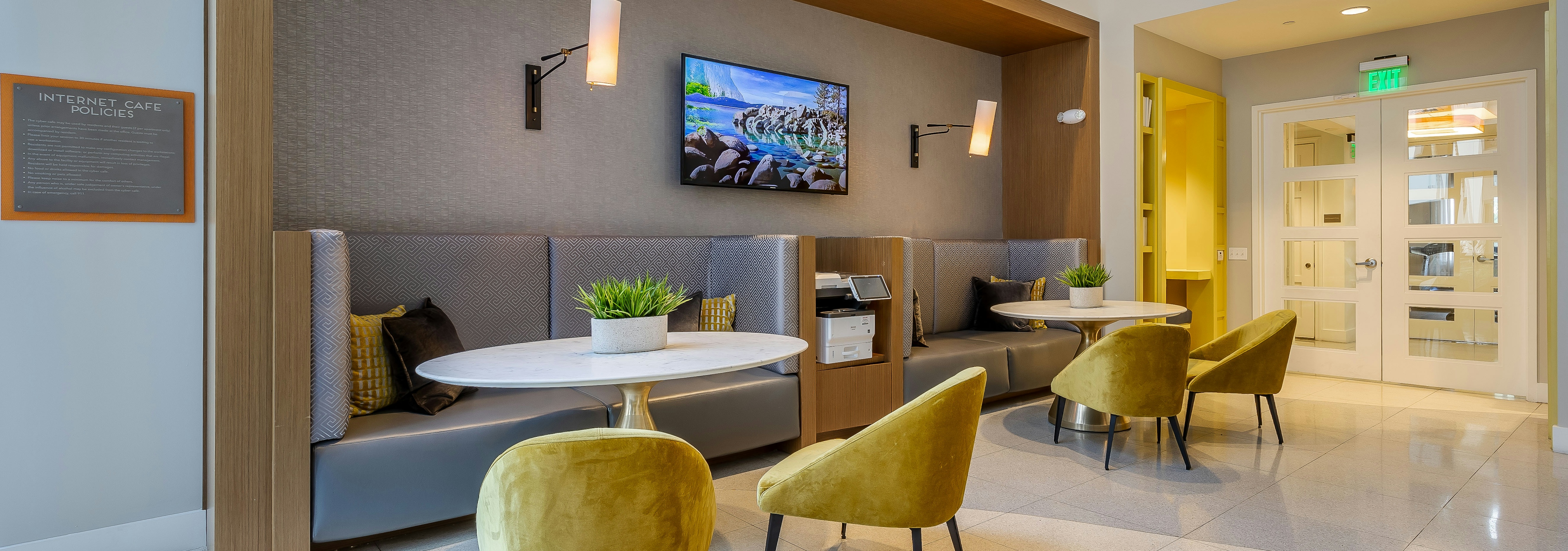 The resident lounge at AMLI 8800 apartments with booth seating and table and yellow chairs with a TV on the wall and sconces