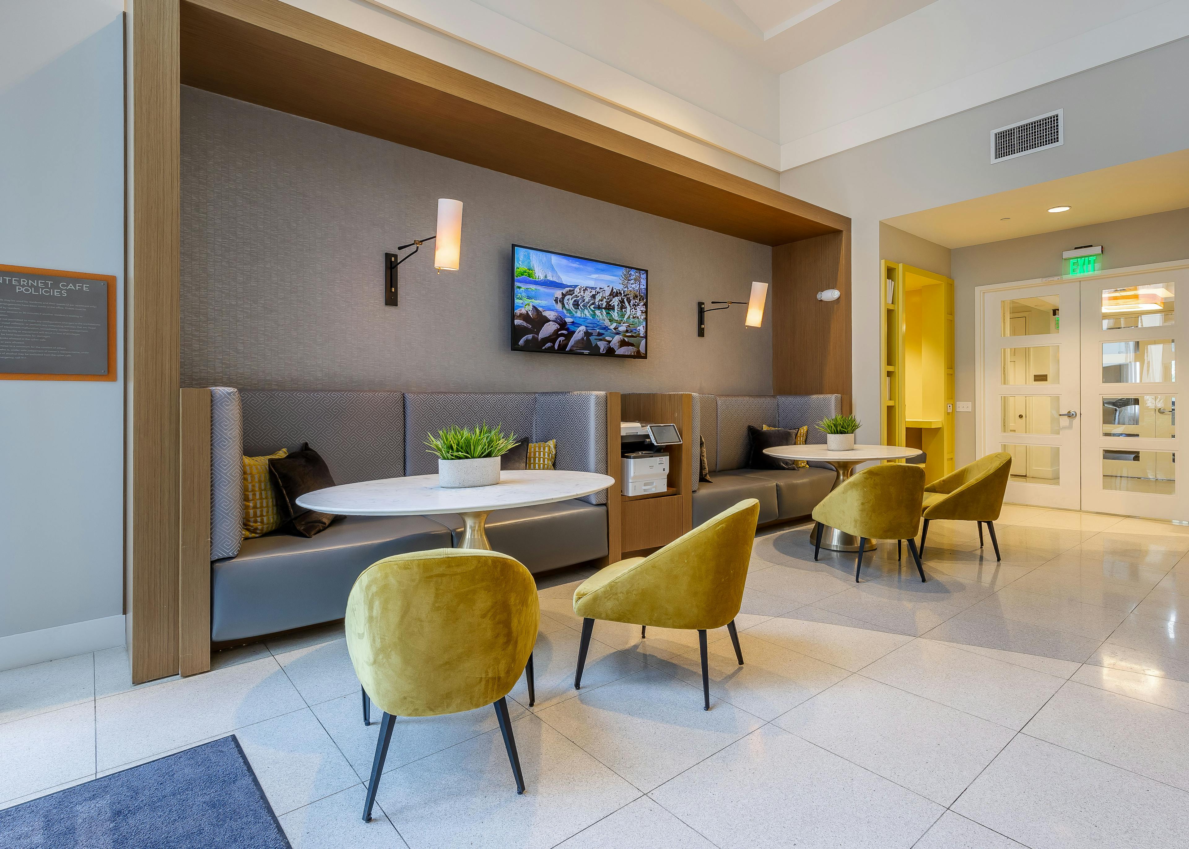 The resident lounge at AMLI 8800 apartments with booth seating and table and yellow chairs with a TV on the wall and sconces 