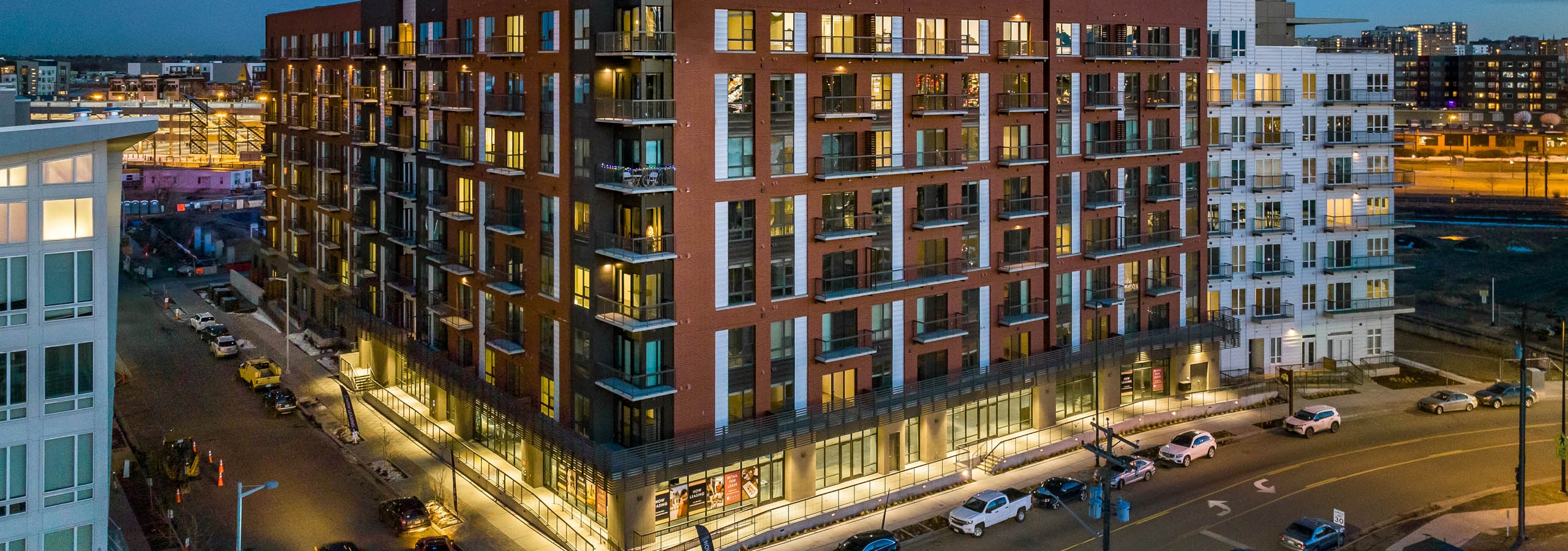 Aerial exterior view of the AMLI Art District building with cars parked along the street with light poles and dark blue sky