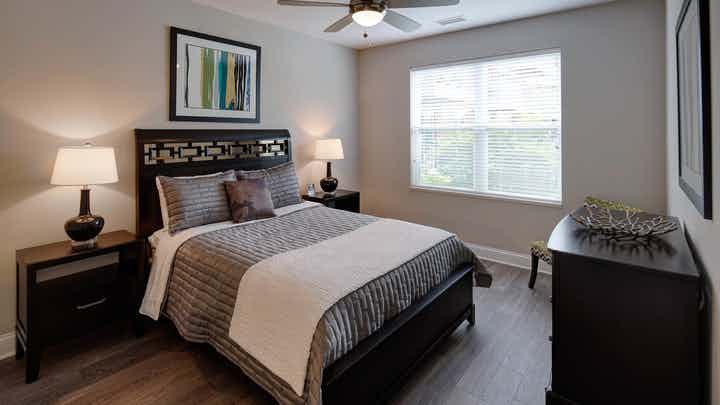 Interior of AMLI Deerfield apartment bedroom with ceiling fan and window furnished with bed and two nightstands and dresser