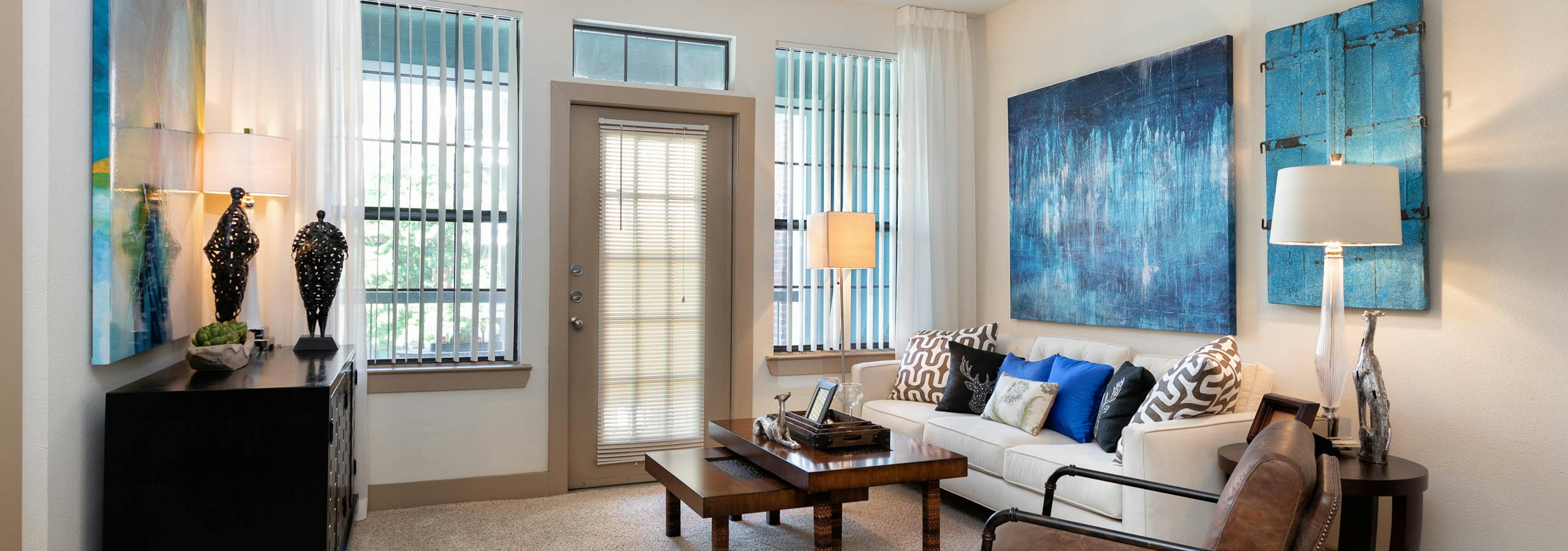 AMLI Eastside living room with two tall windows on either side of a balcony door with white walls and beige carpeting