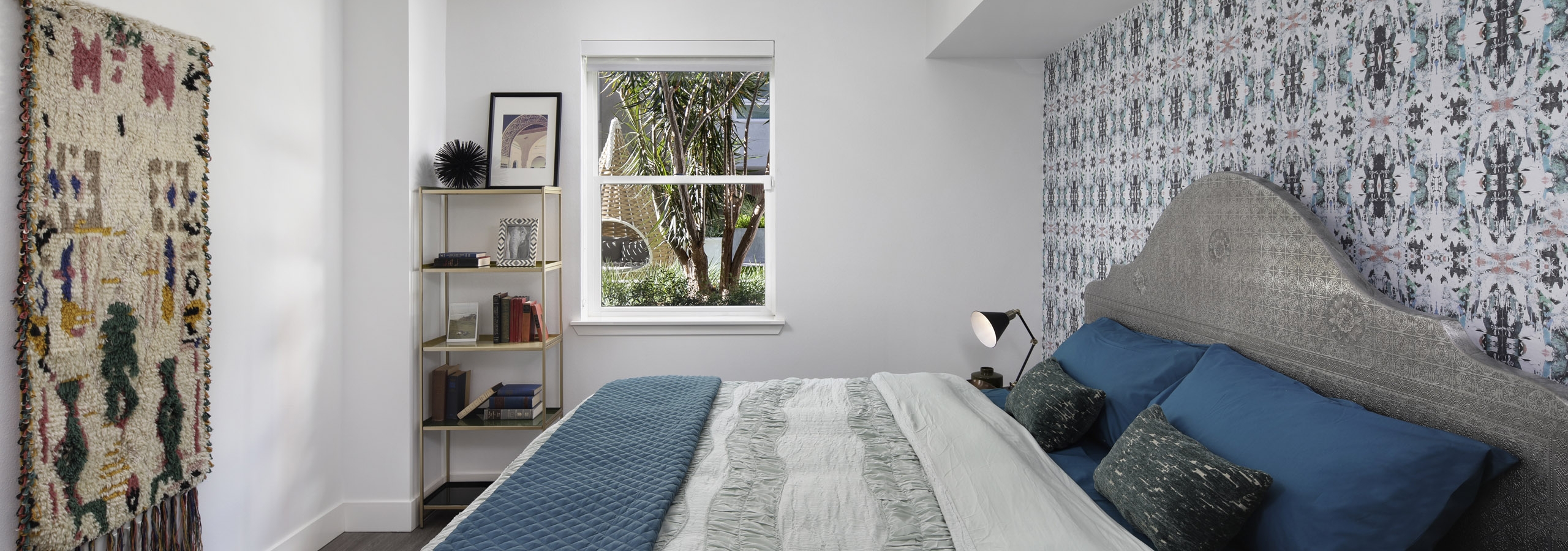 AMLI Park Broadway master bedroom with boho chic décor and designer wallpaper behind a king size bed with blue sheets