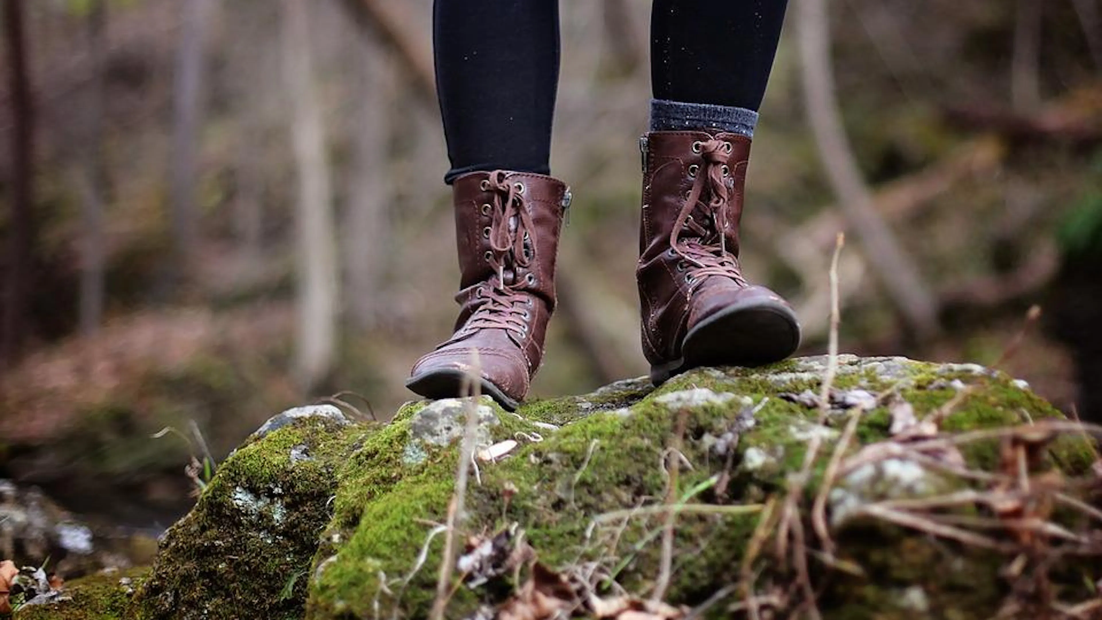 Close up of a pair of boots standing on a moss covered rock in a forest