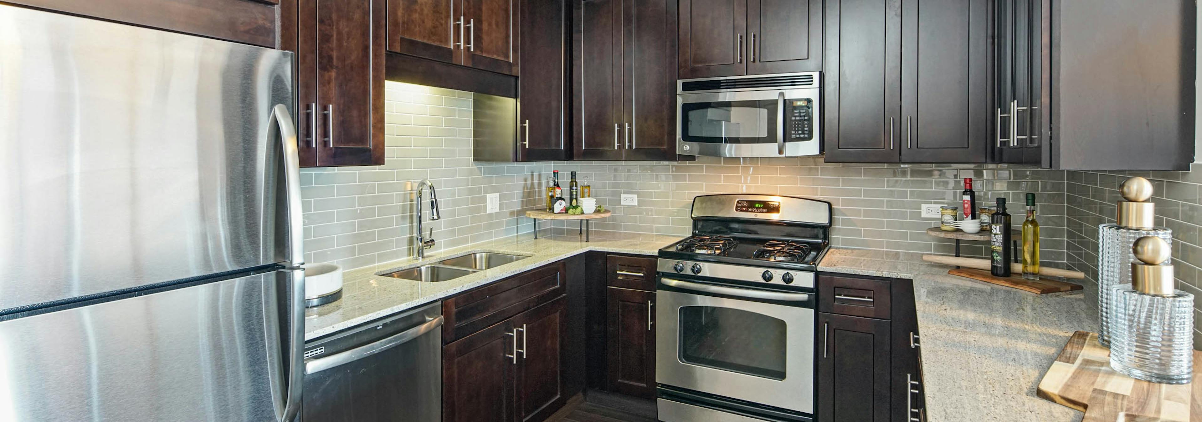 AMLI River North apartment kitchen with dark wood cabinets and granite countertops featuring stainless steel appliances