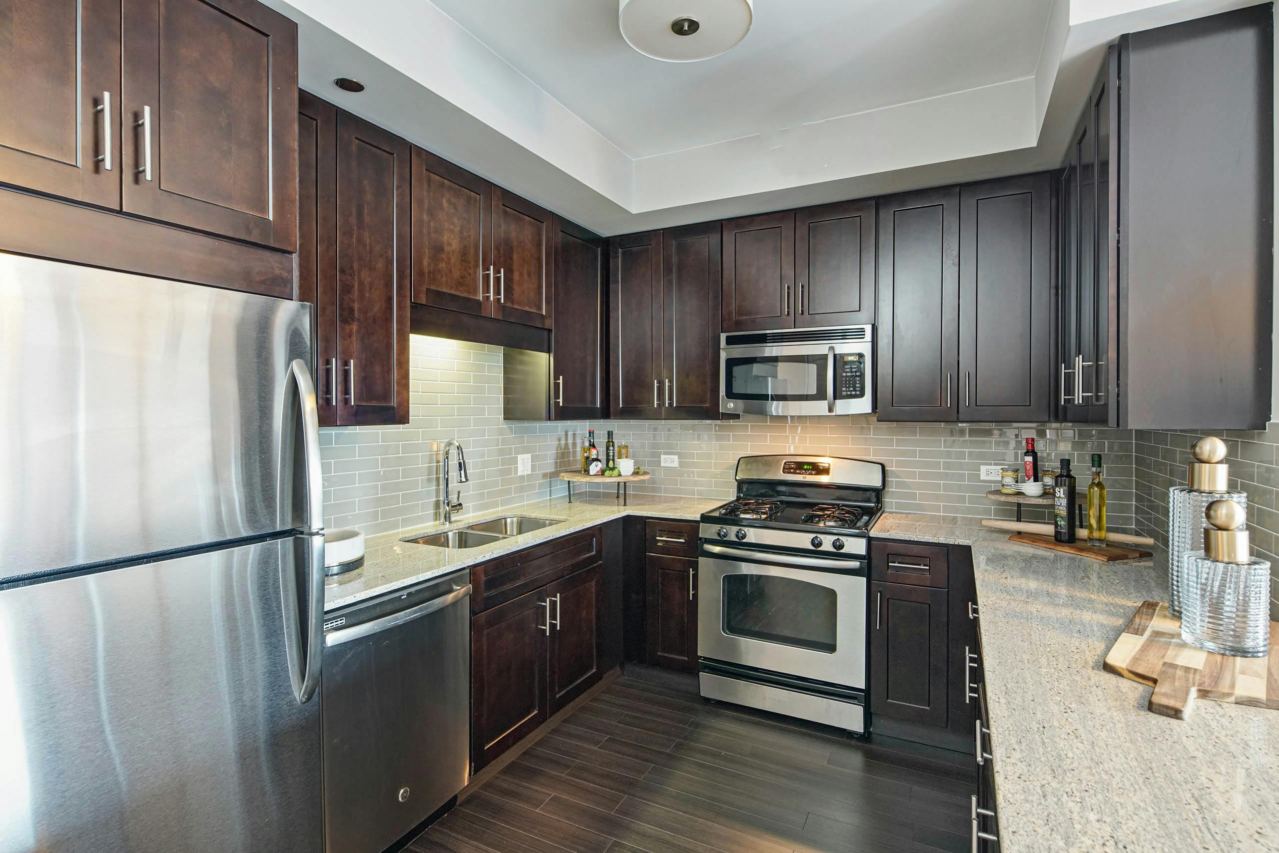 AMLI River North apartment kitchen with dark wood cabinets and granite countertops featuring stainless steel appliances