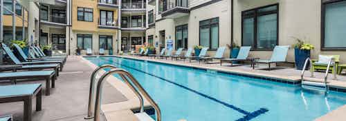 Exterior close up of swimming pool water at AMLI 5350 surrounded by blue lounge chairs and apartment building facade