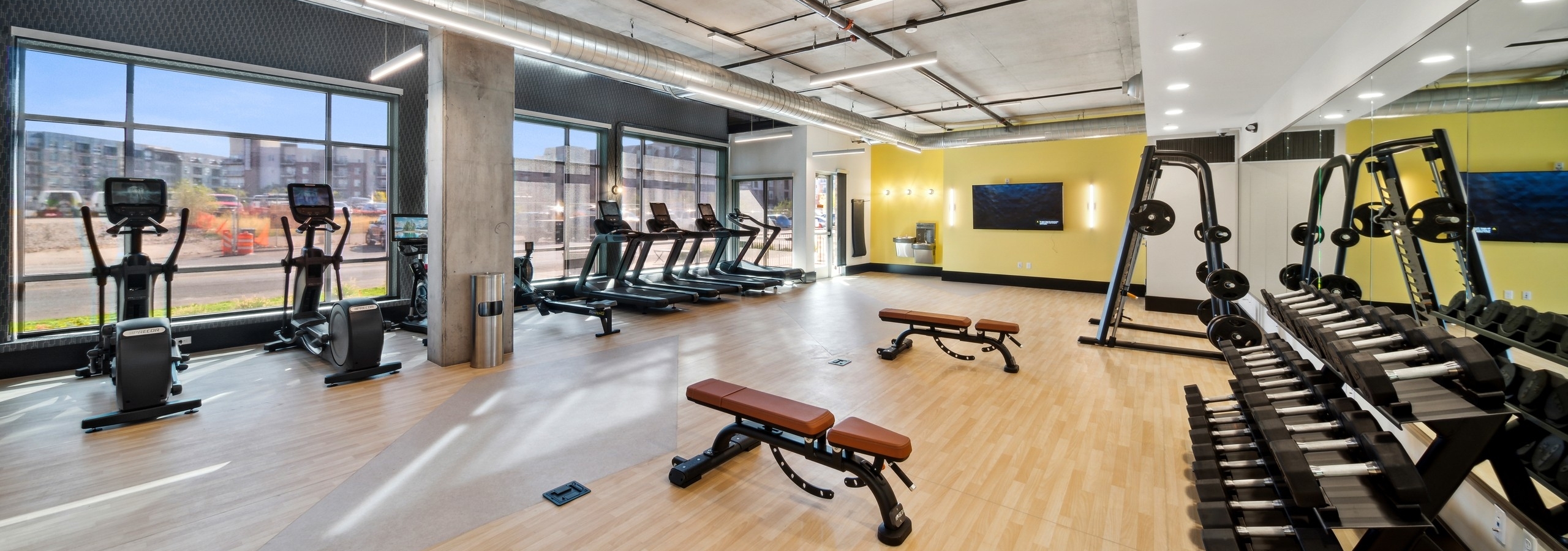 AMLI RiNo fitness center with treadmills on window wall with mirrored wall and weightlifting equipment and wood floors