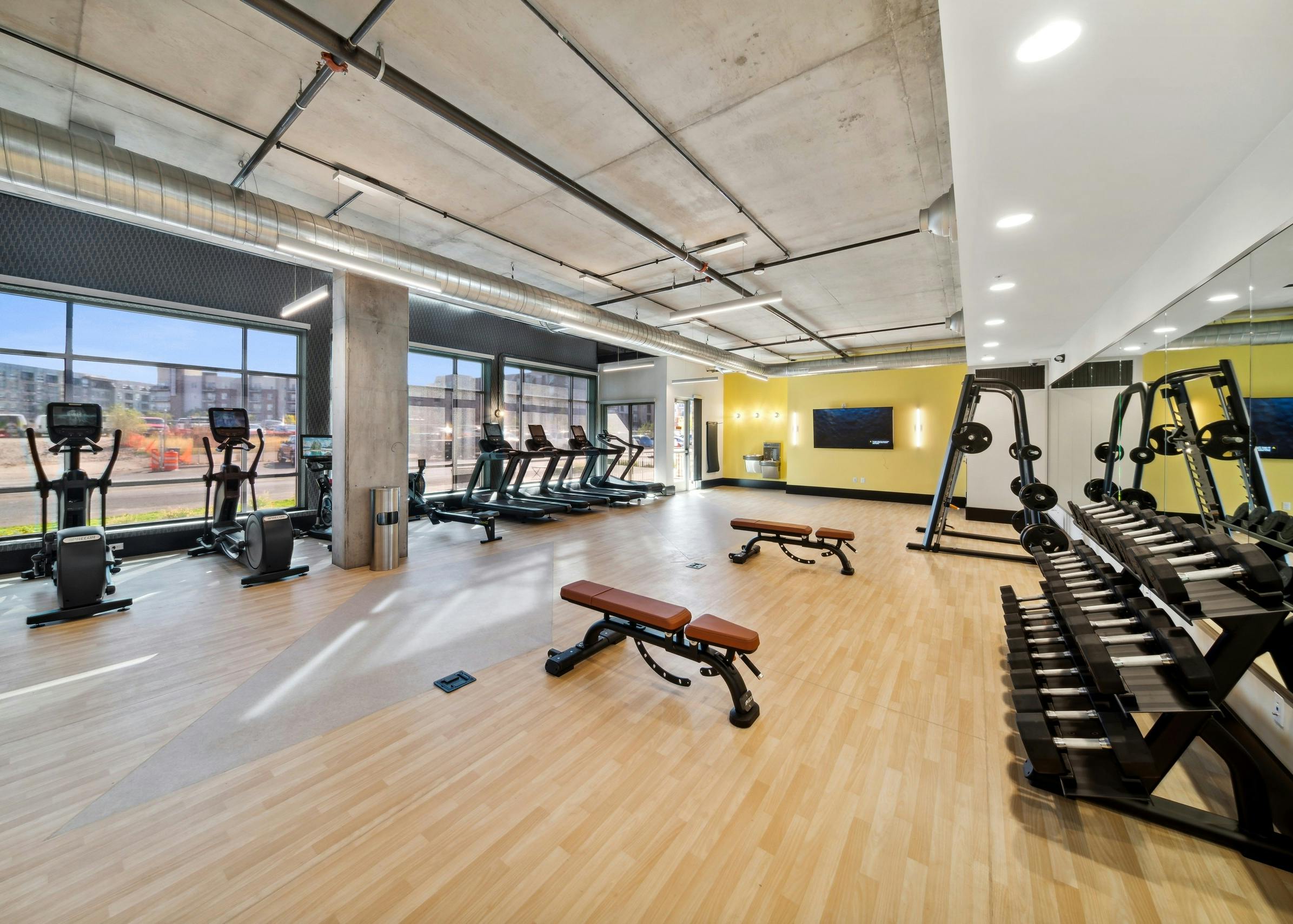 AMLI RiNo fitness center with treadmills on window wall with mirrored wall and weightlifting equipment and wood floors