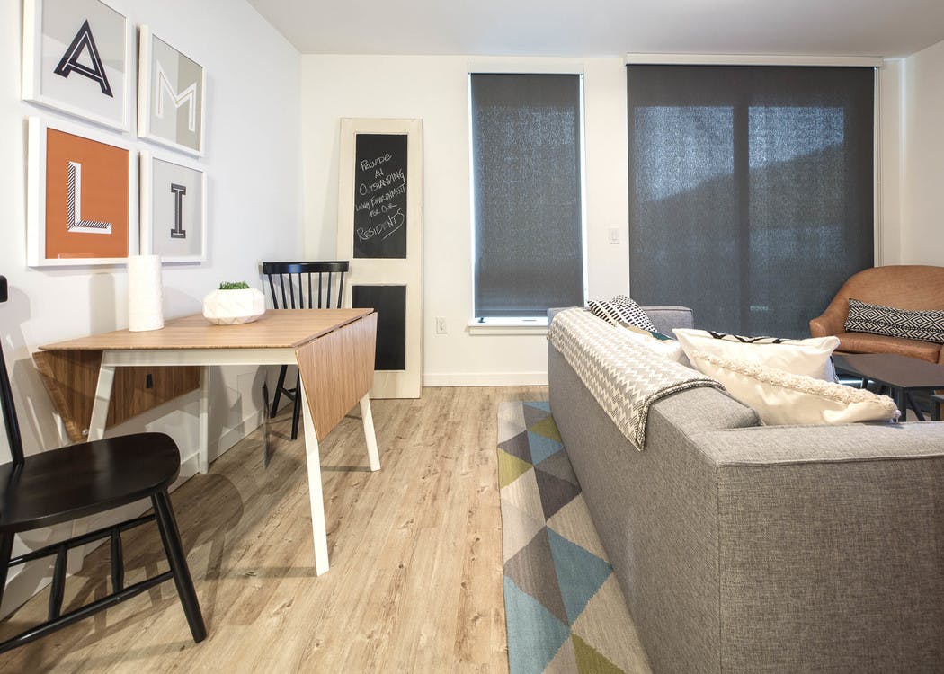 Interior AMLI Wallingford apartment living room with kitchen table and two chairs with a grey couch and solar shades