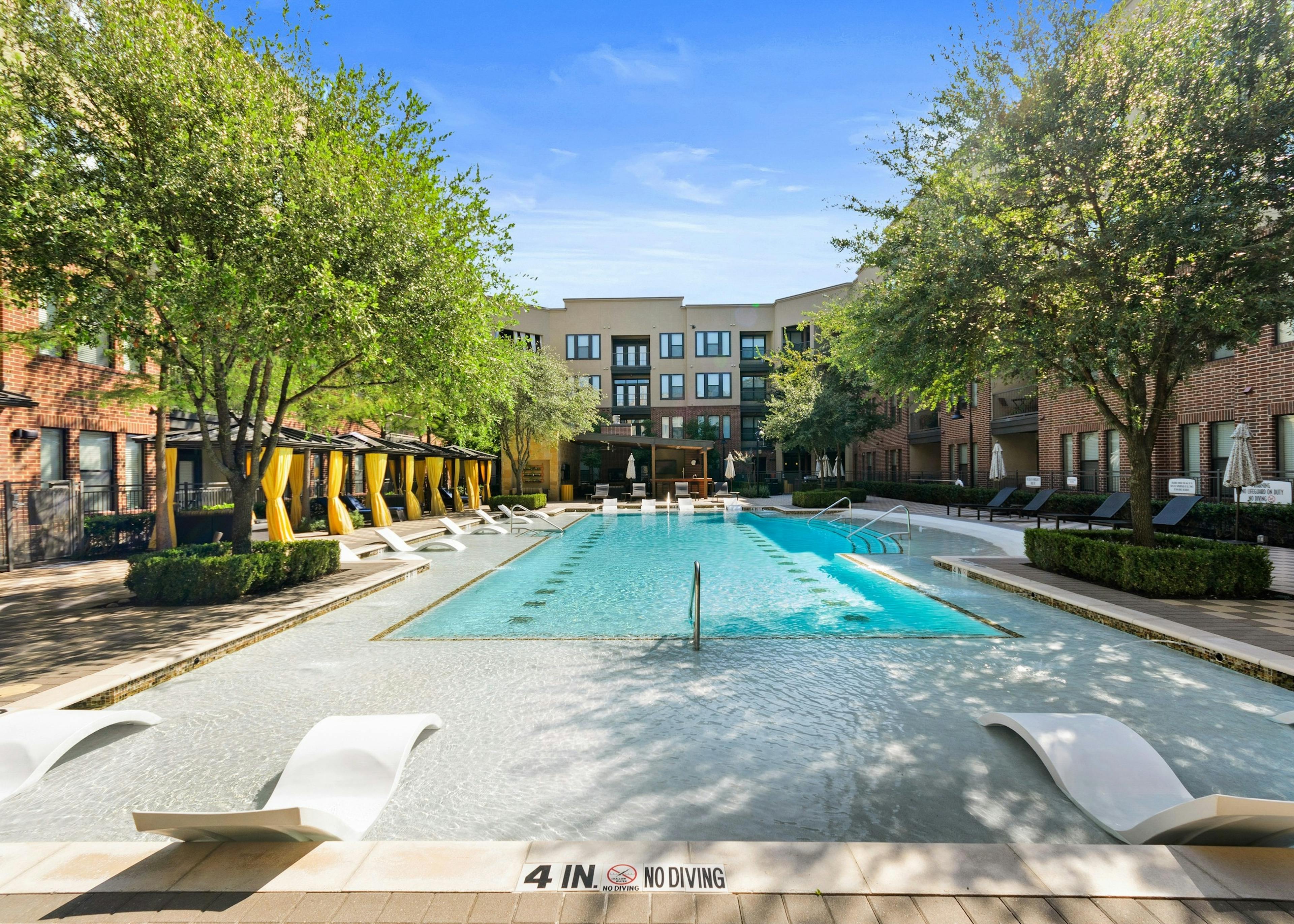 Courtyard pool at AMLI West Plano apartments featuring in water seating and surrounded by lush landscaping and lounge seating