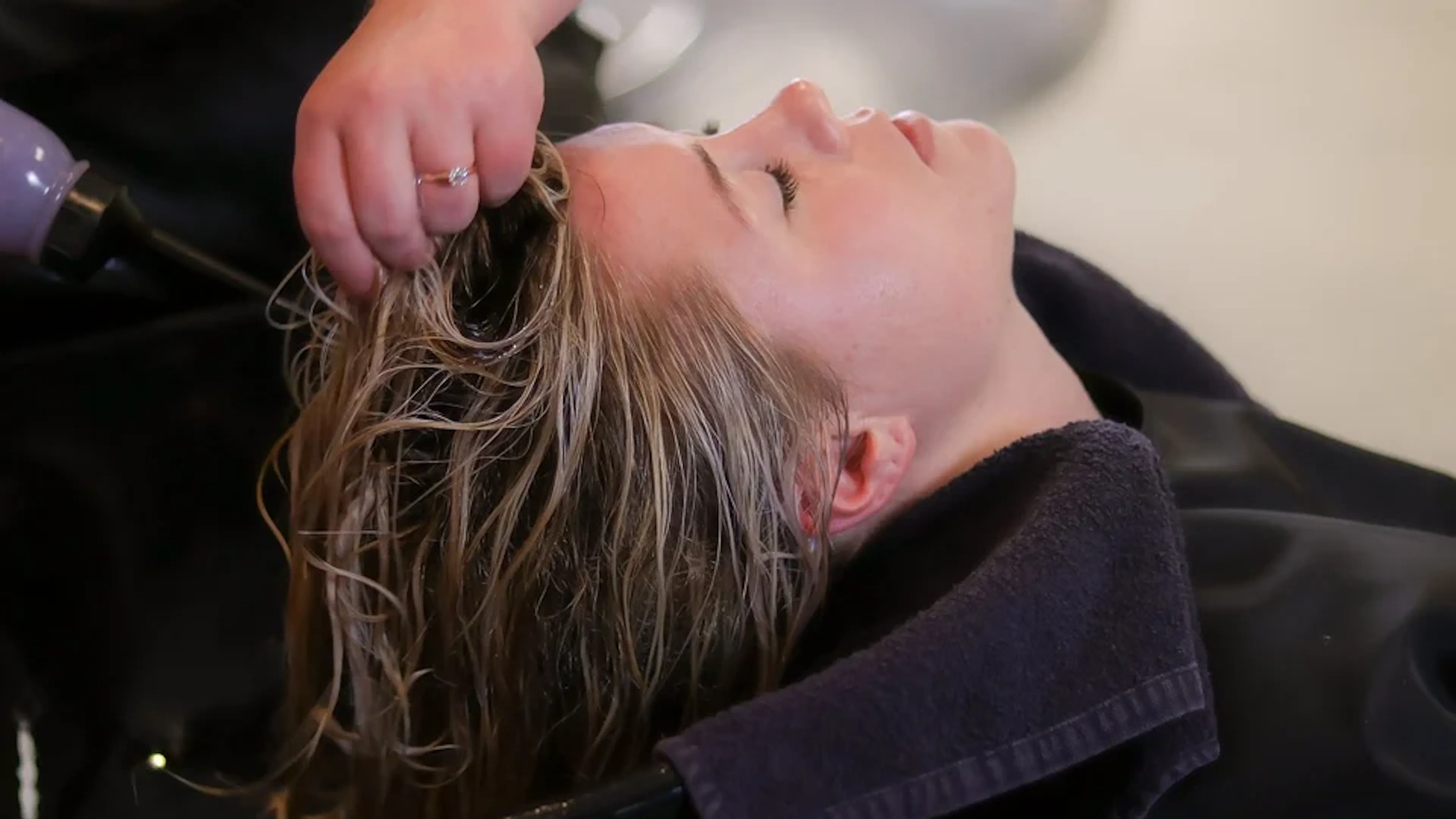 A blonde woman getting her hair washed over a salon sink
