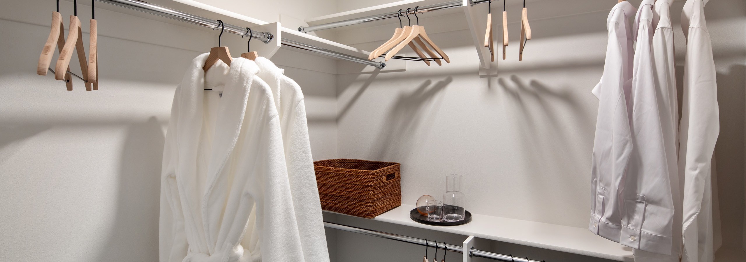View of master bedroom closet with and hanging rods and bathrobes and shirts hanging from wooden hangers at AMLI Old Pasadena