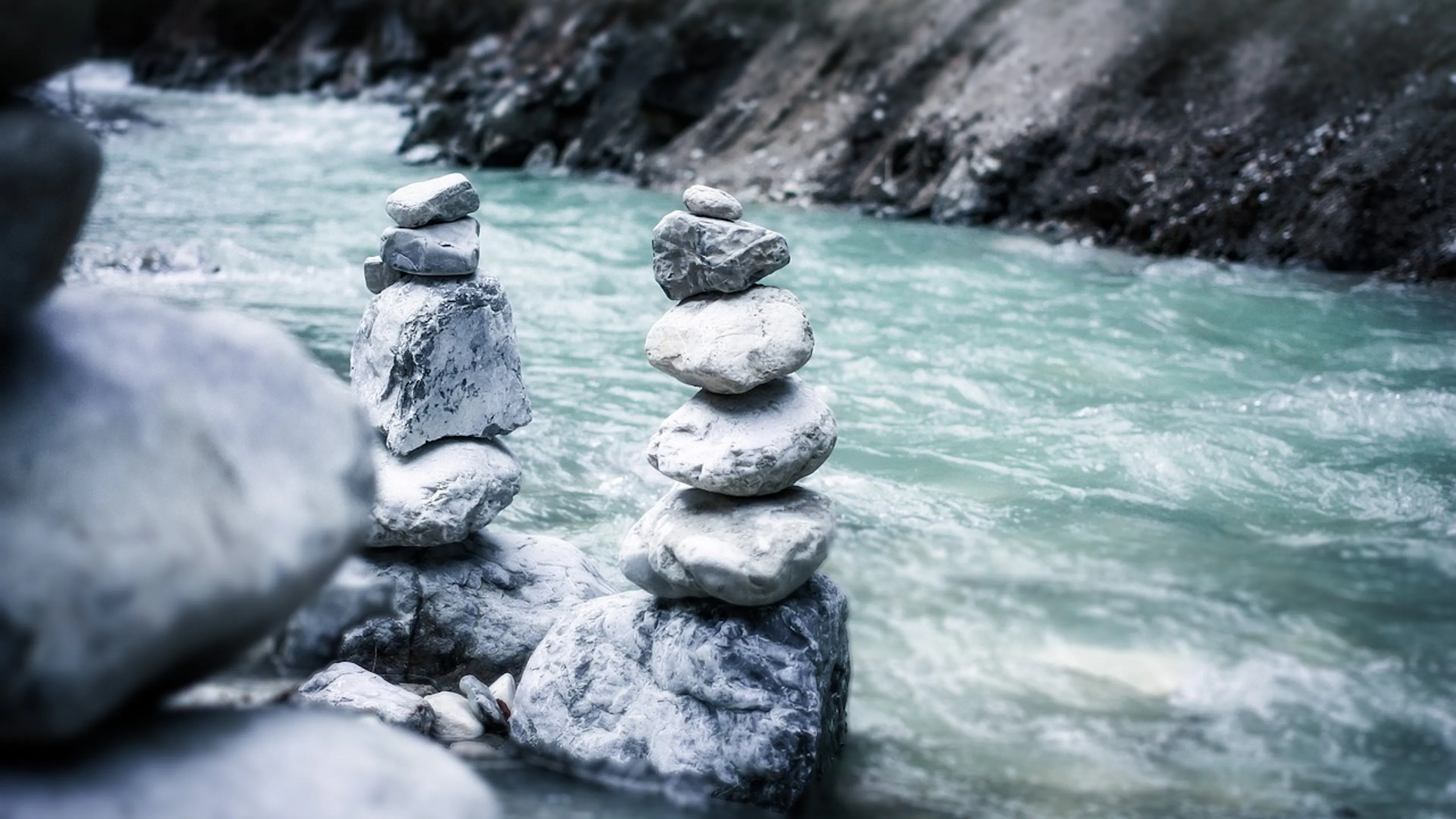 Rocks stacked in two piles in front of blue-green rushing river water