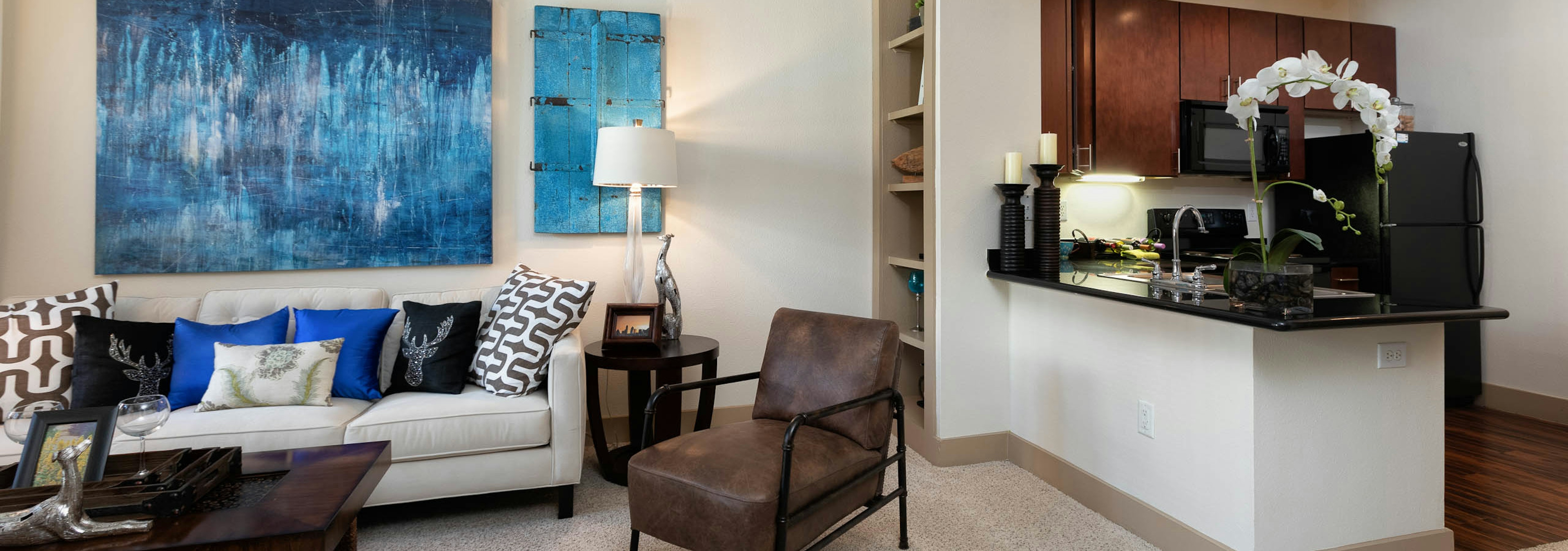 Living room at AMLI Eastside with large blue wall art above a white sofa with a built in bookshelf and carpeted flooring