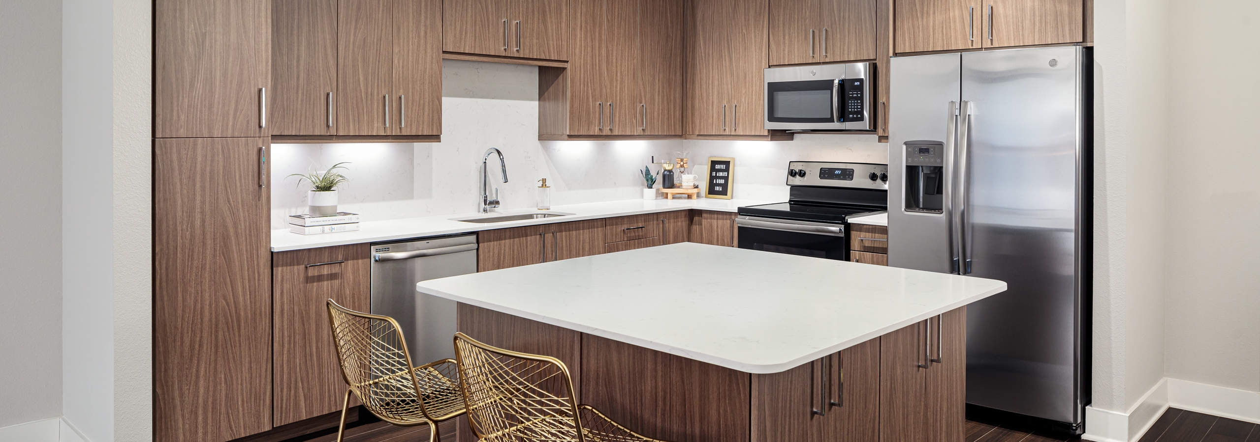 Interior of island kitchen at AMLI Addison with light wood cabinets and white countertops with stainless steel appliances