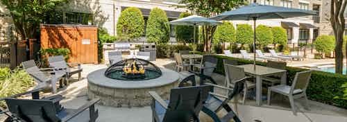 AMLI Las Colinas poolside stone circular fire pit encircled by 9 gray Adirondack chairs and nearby grill and tables and chairs