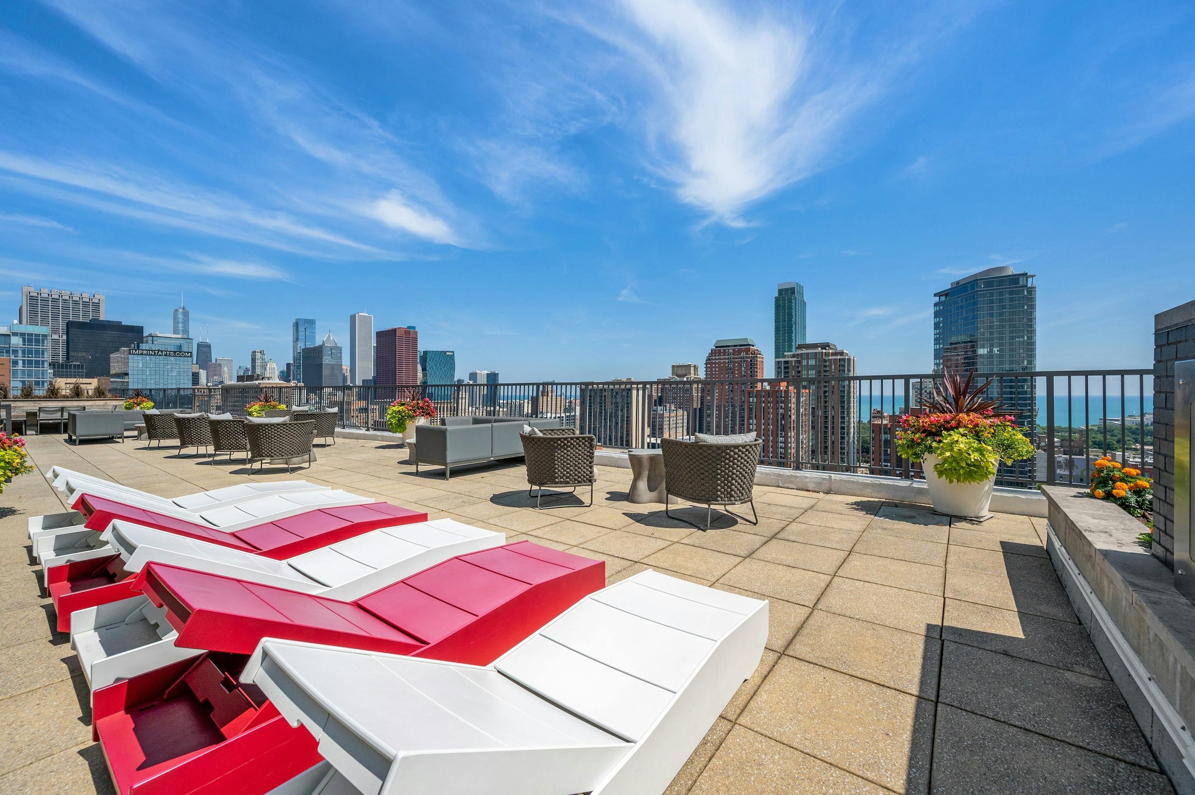 Rooftop with view of skyline at AMLI 900 with red and white wood lounge chairs and flower planters with chairs and tables