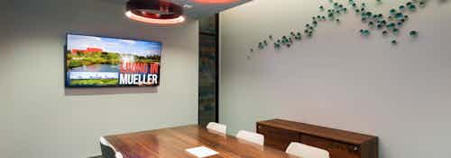 Interior view of conference room at AMLI on Aldrich with large wooden desk and a flat screen TV hanging on neutral wall