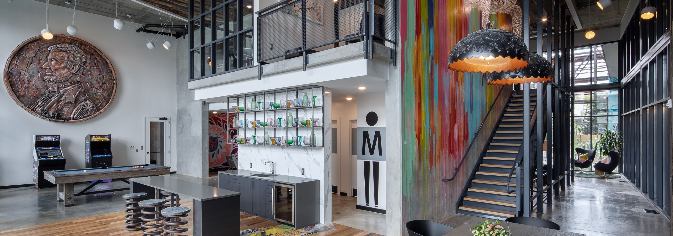 AMLI Westside resident lounge with concrete floors and high ceilings with penny artwork on wall and stairs to business center