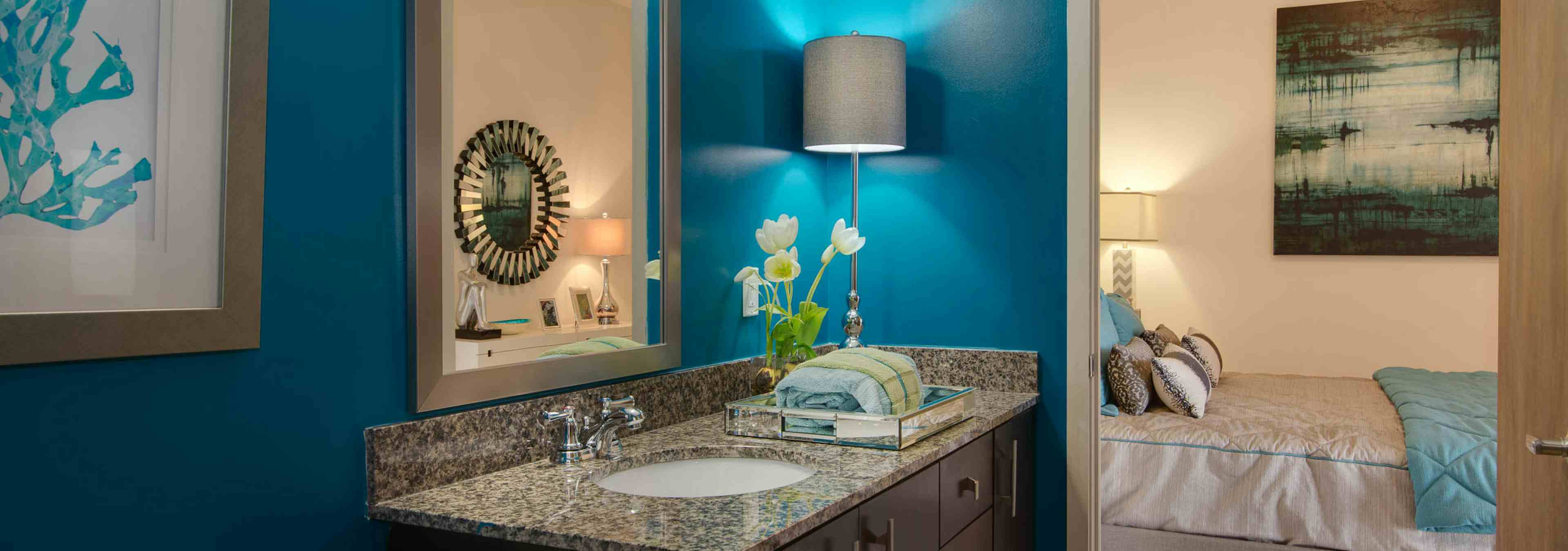 AMLI Old 4th Ward apartment bathroom with granite countertops and dark cabinetry with blue walls and a peek into the bedroom