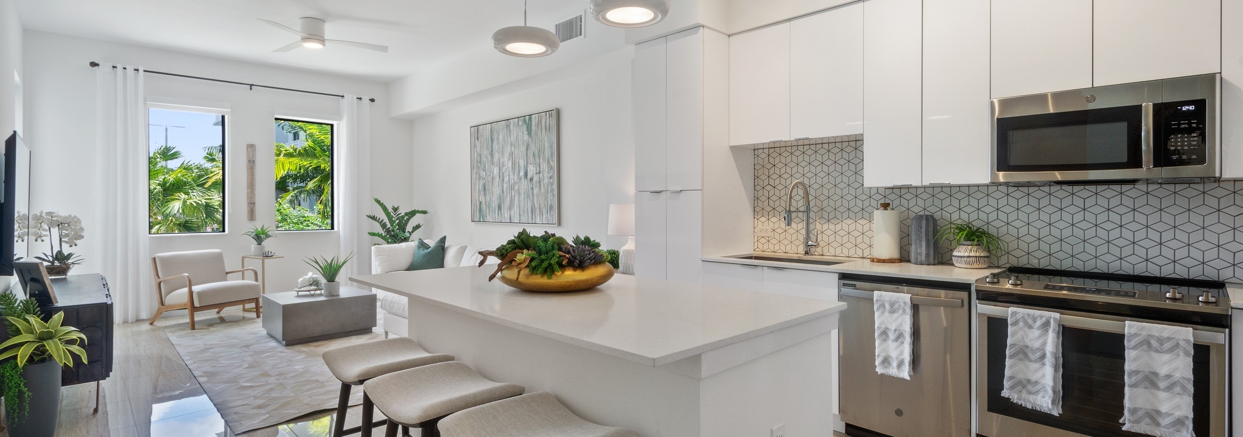 Kitchen at AMLI Park West apartments with white cabinets and island with stools and a peek into living area with side window
