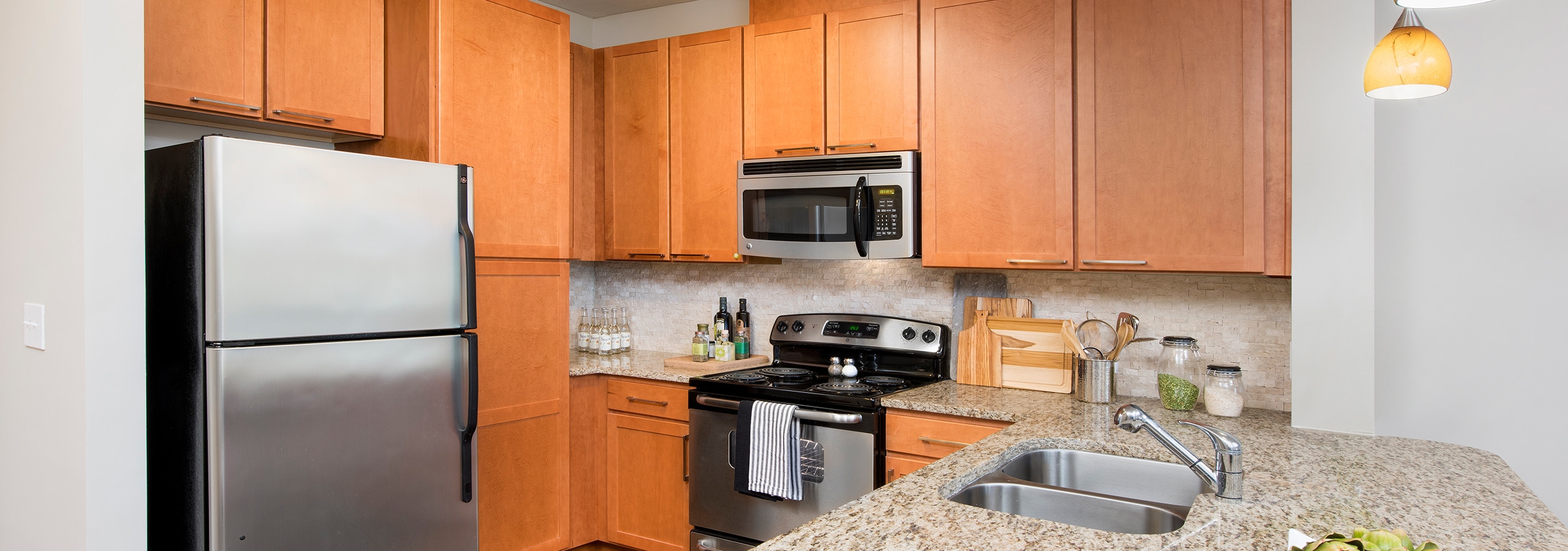 AMLI North Point kitchen with medium colored wood cabinets and stainless steel appliances with spacious granite countertops