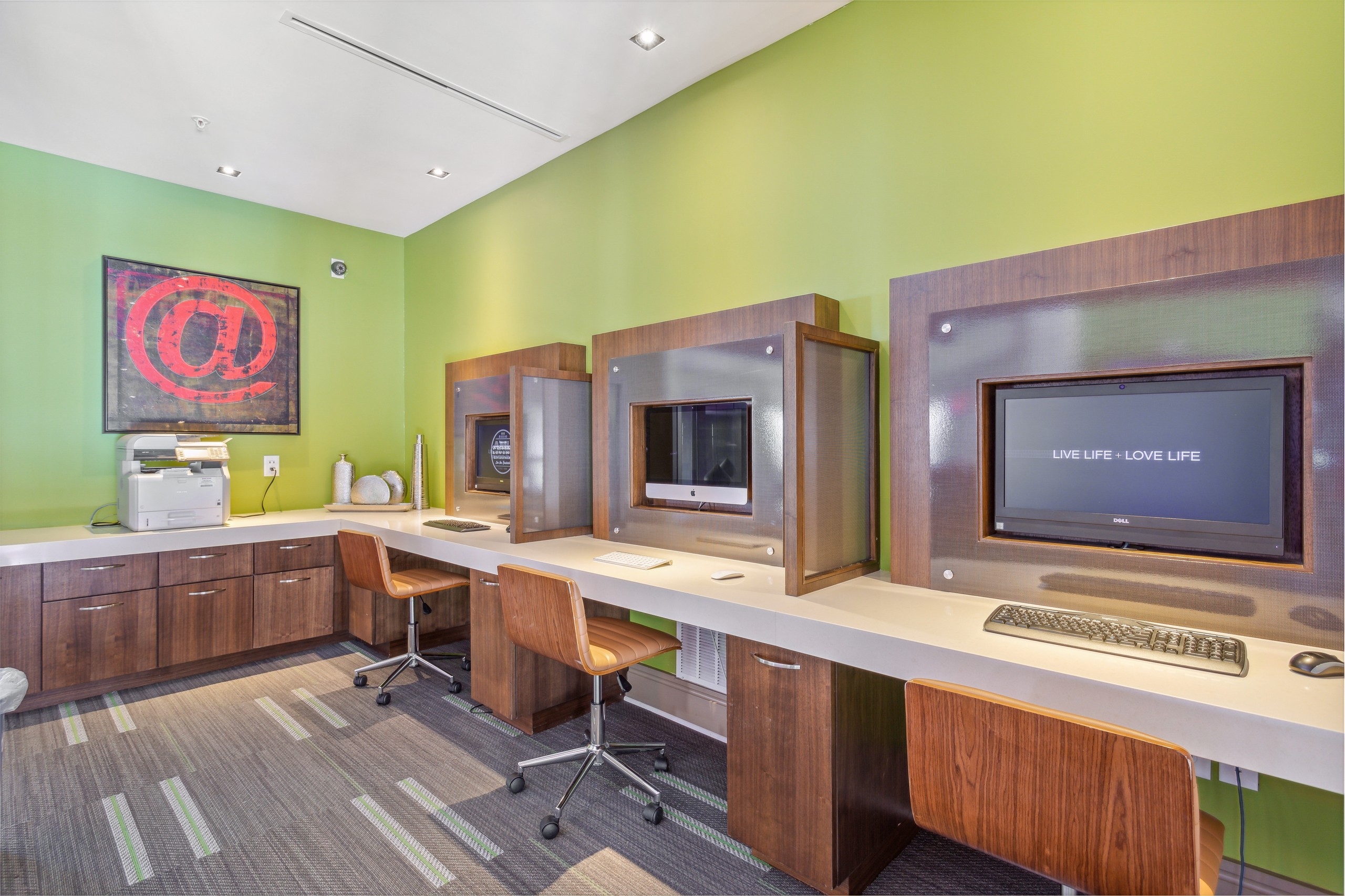 AMLI Ponce Park business center with 3 computer stations with brown wheeled chairs and a printer and bright green walls