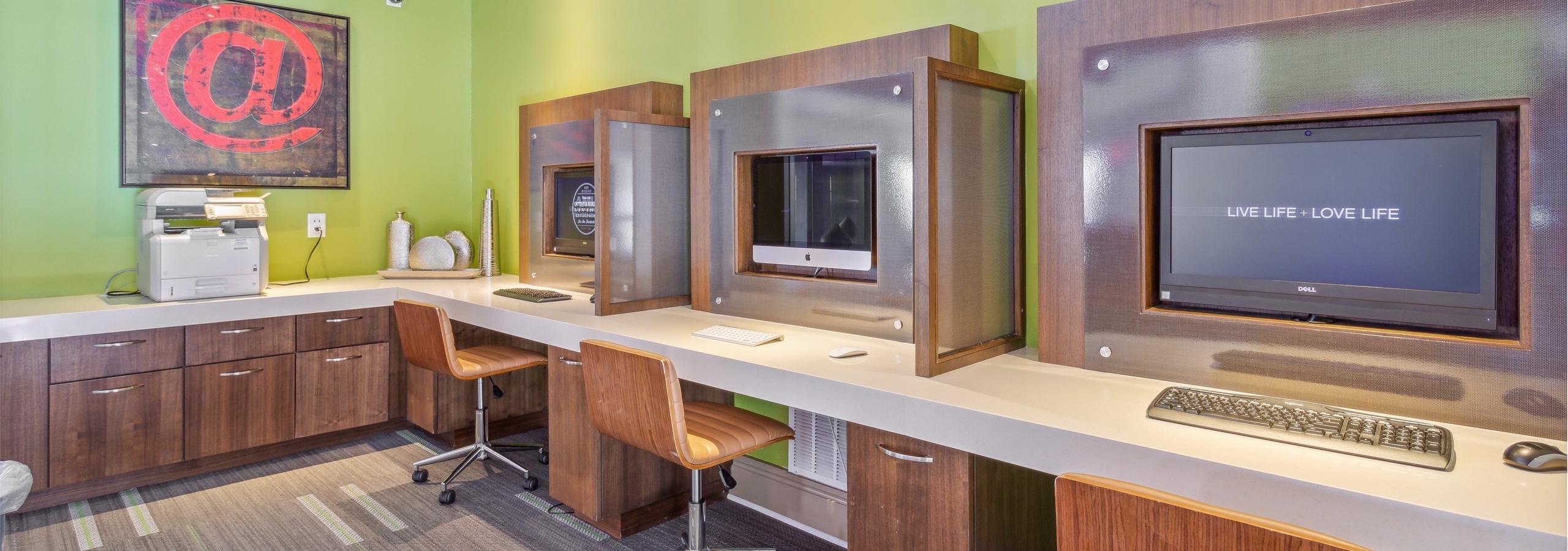AMLI Ponce Park business center with 3 computer stations with brown wheeled chairs and a printer and bright green walls