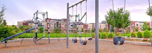 A playground in the surrounding area of AMLI Arista apartments with swings and a jungle gym and landscaped with wood chips