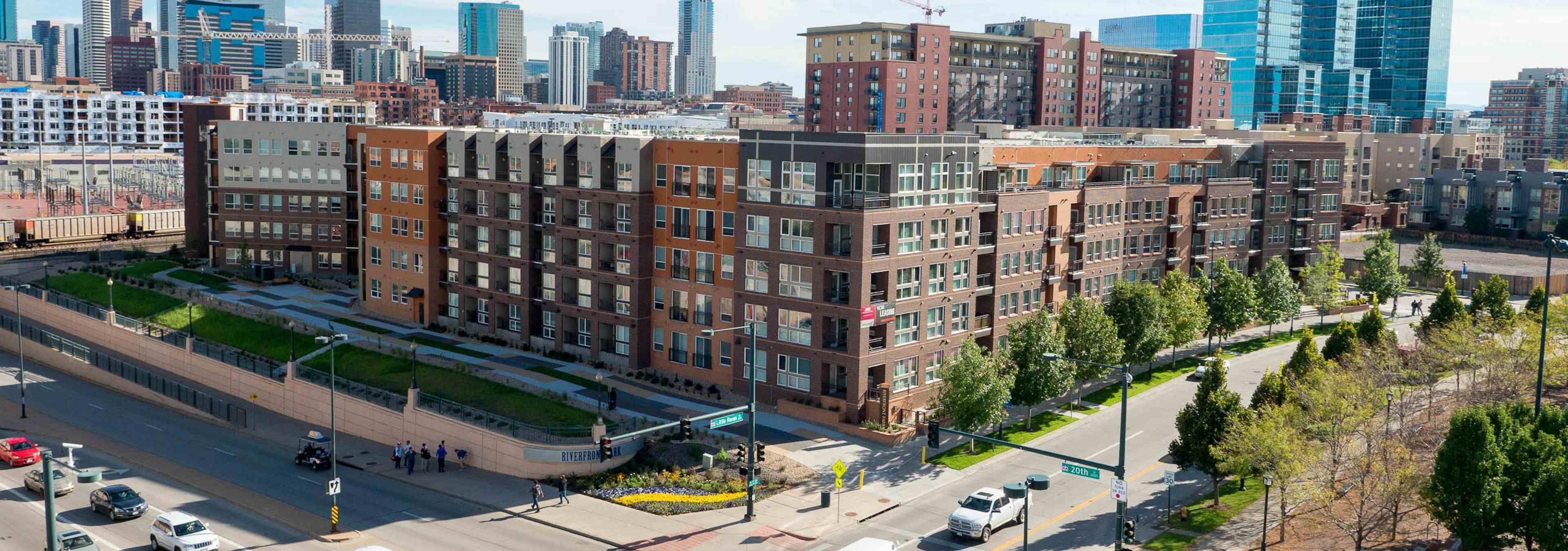 Ariel view of AMLI Riverfront Park apartments with downtown Denver in the background with cars and people on the sidewalk