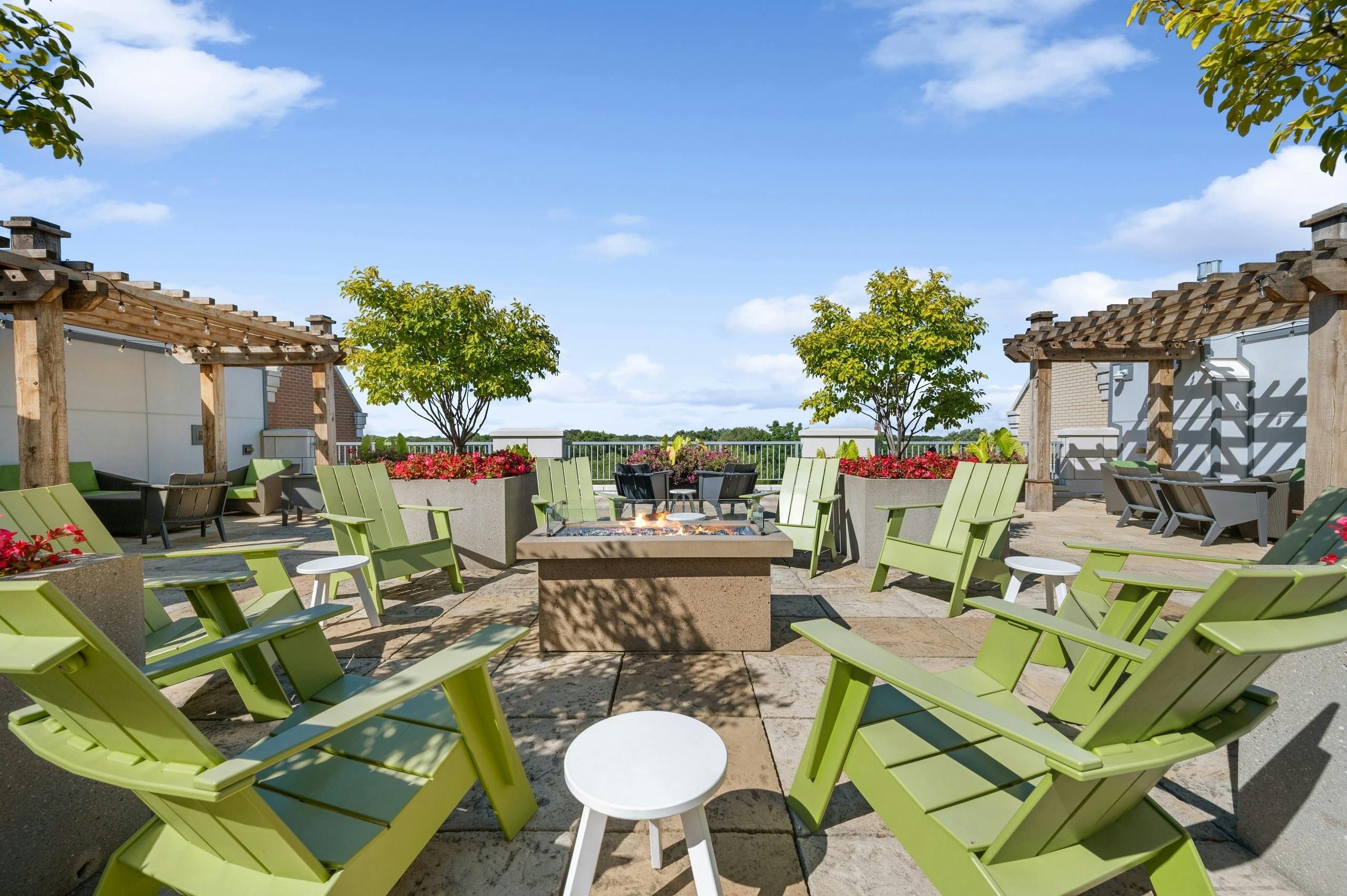 AMLI Evanston rooftop with green Adirondack chairs surrounding lit firepit with pergolas and potted trees and flowers